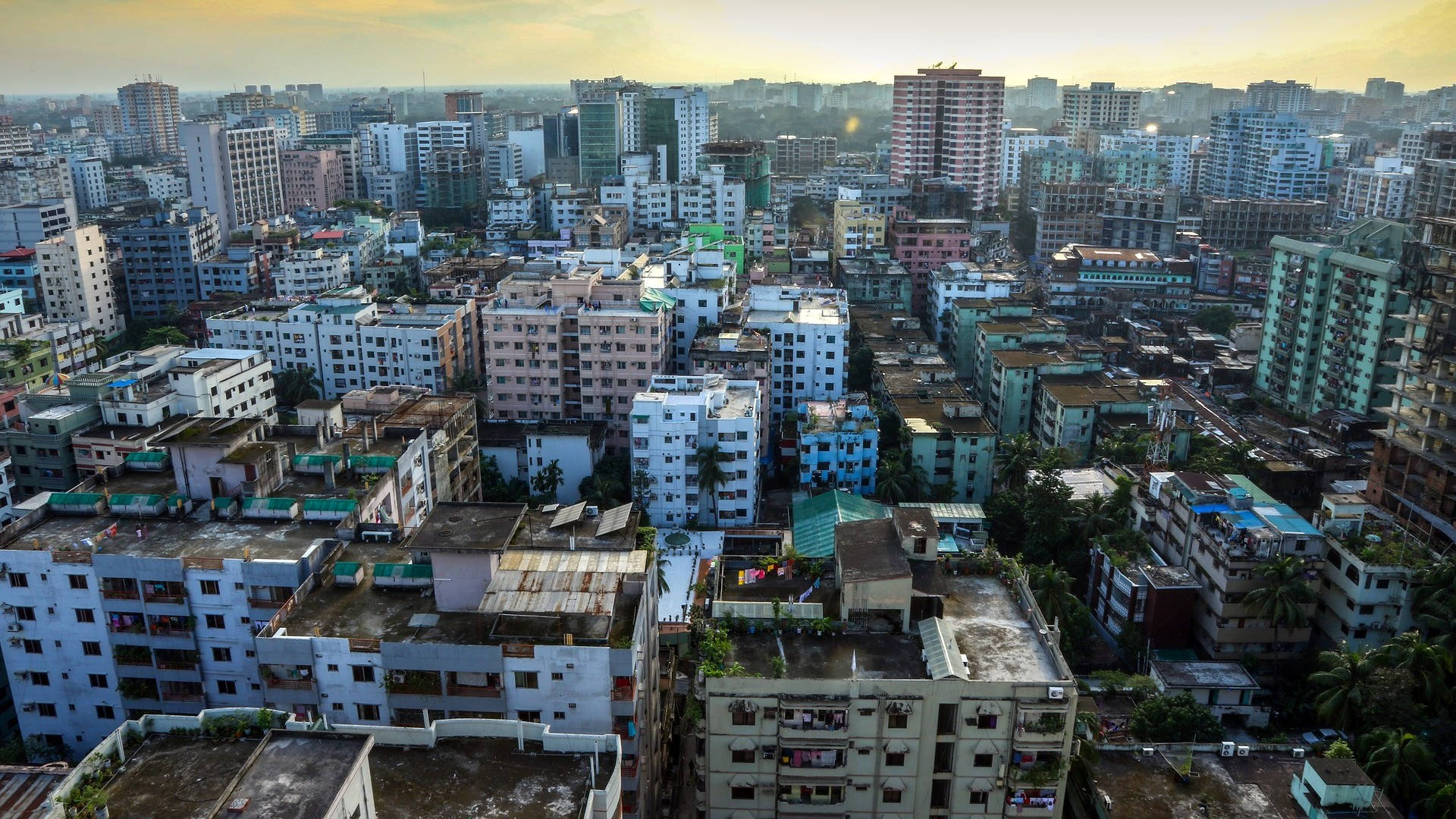 Bangladesh 桌布 壁紙 — 溫暖天空下，黃金時段密集城市擴張中混合高層和低層建築的鳥瞰圖。