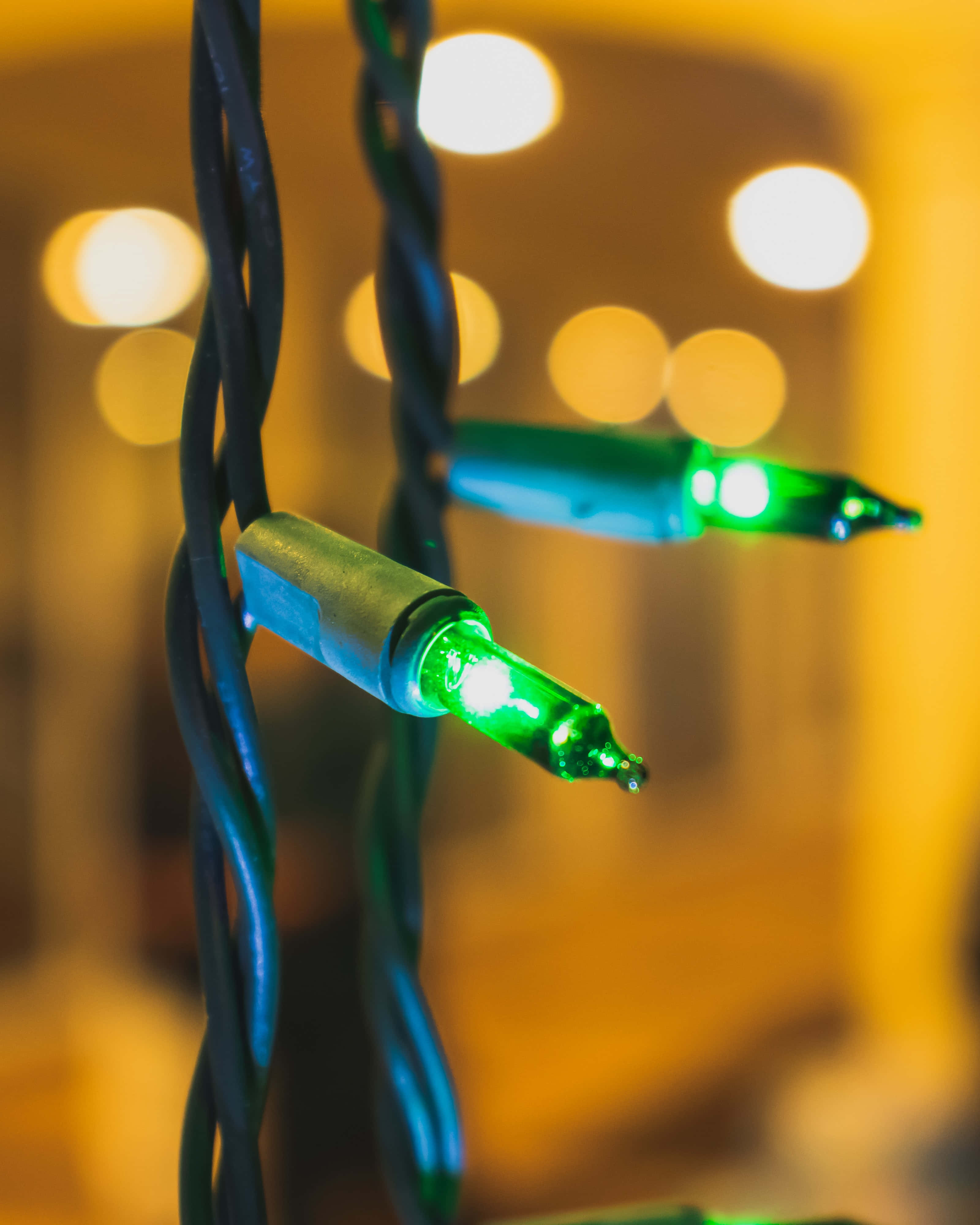 Christmas Light 桌布 壁紙 — 溫暖散景背景下發光綠色串燈的特寫，帶有扭曲的黑色電線。
