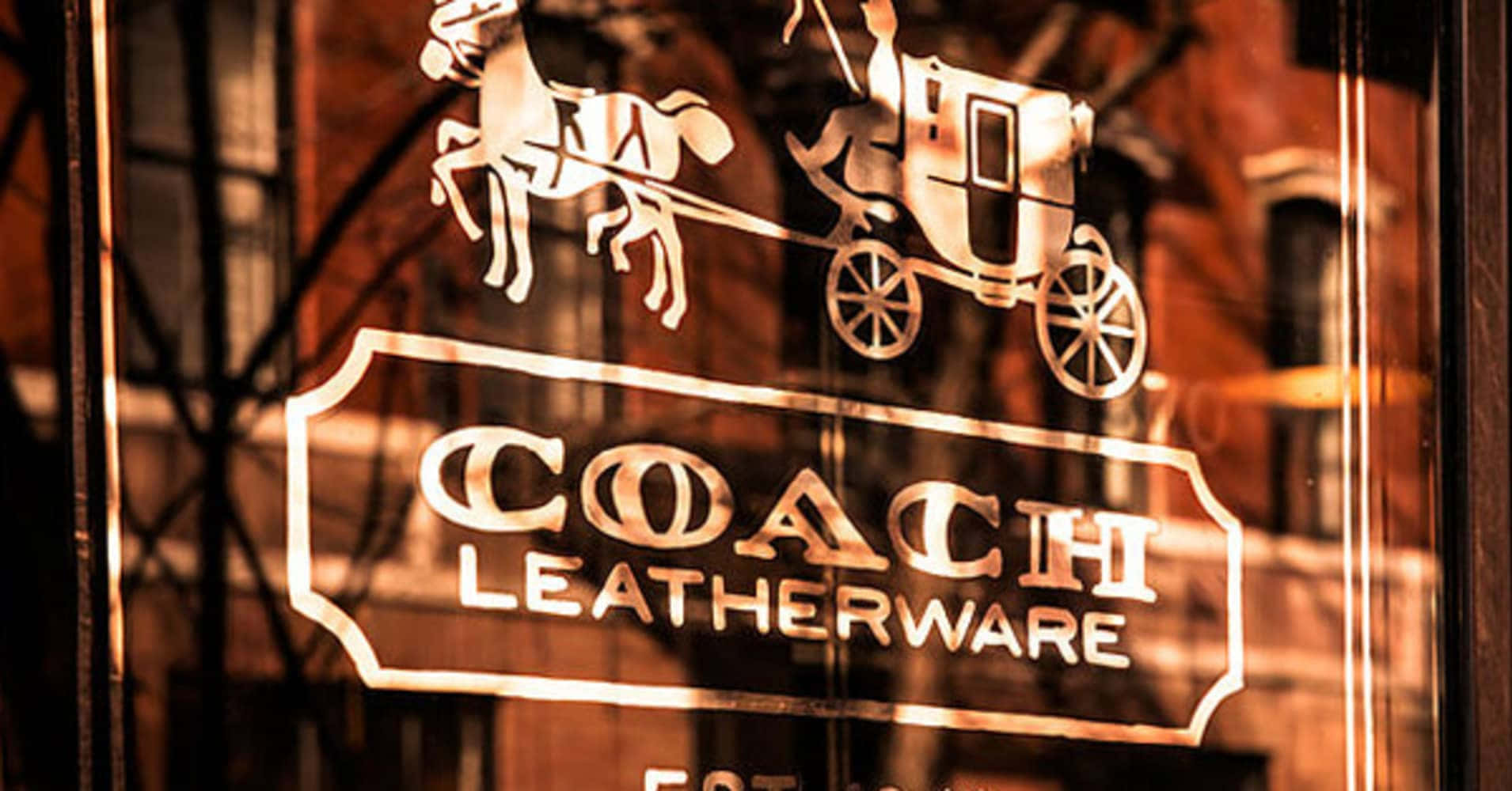 Coach 桌布 壁紙 — 溫暖照明的Coach皮革製品店招牌，玻璃上蝕刻著馬車，在黃昏時反射出磚砌建築。