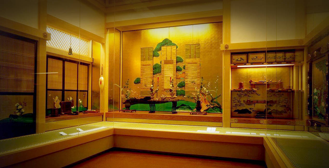 Nagoya 桌布 壁紙 — 溫暖照明的傳統日本博物館展覽，展示金色屏風、花卉佈置及玻璃櫃下的漆器工藝品。