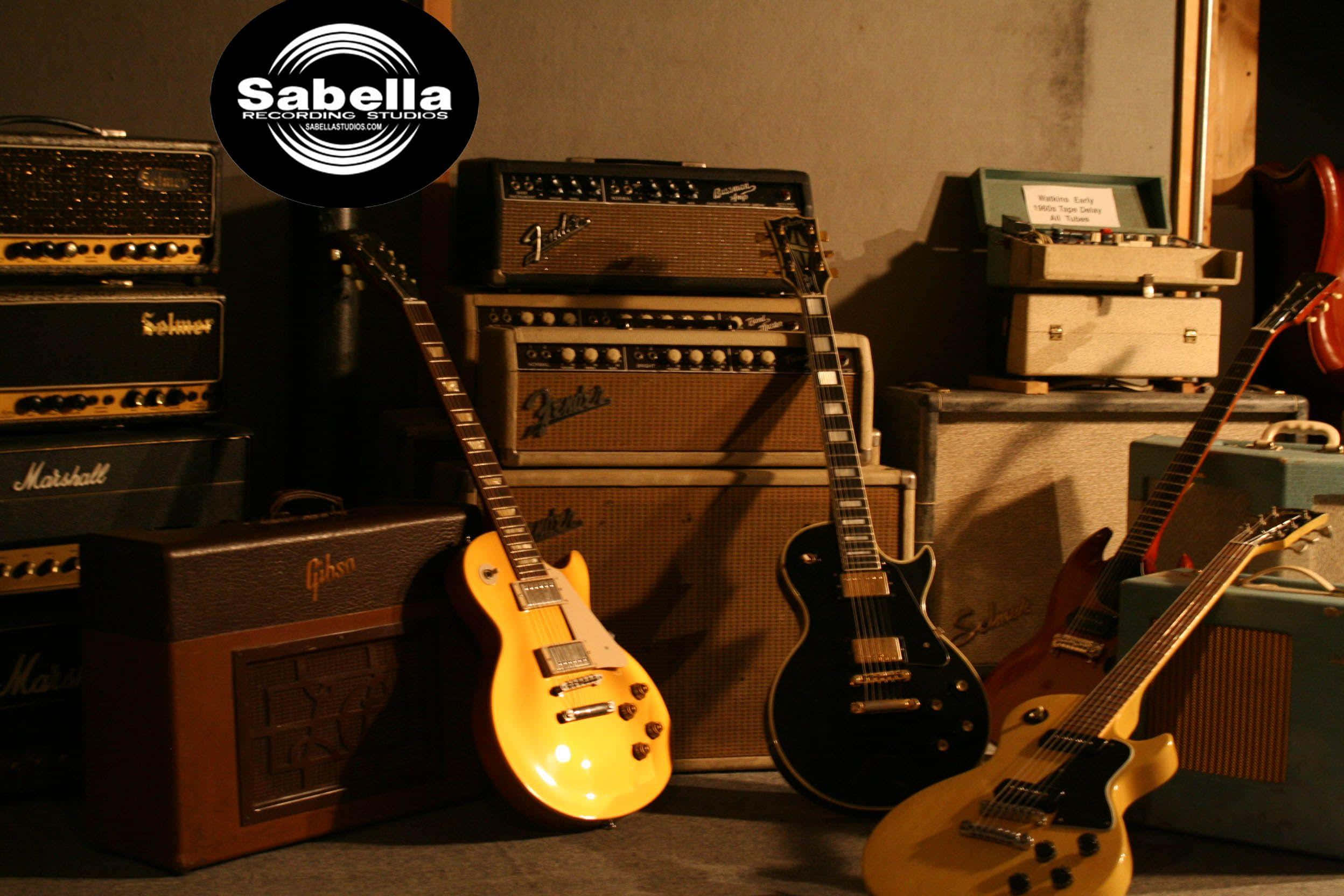 Guitar Amp 桌布 壁紙 — 溫暖照明的復古吉他和擴音器靠在堆疊的設備上，位於舒適的錄音室中。