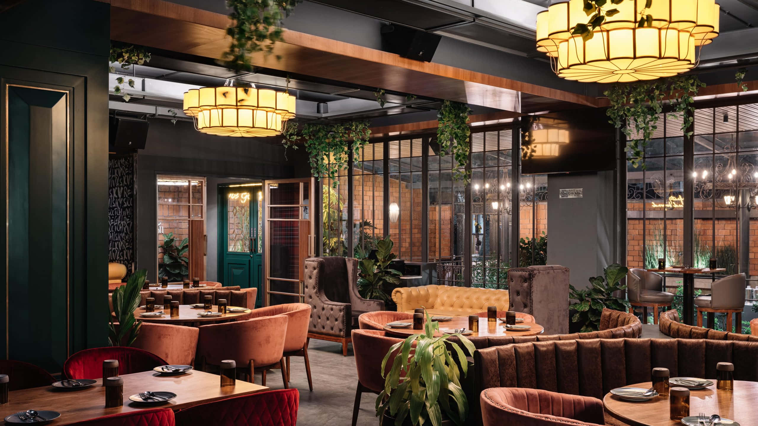 Pub 桌布 壁紙 — 溫暖照明的現代餐廳，配有豪華天鵝絨椅子、木桌、吊燈和茂密的綠色植物，營造出溫馨舒適的氛圍。