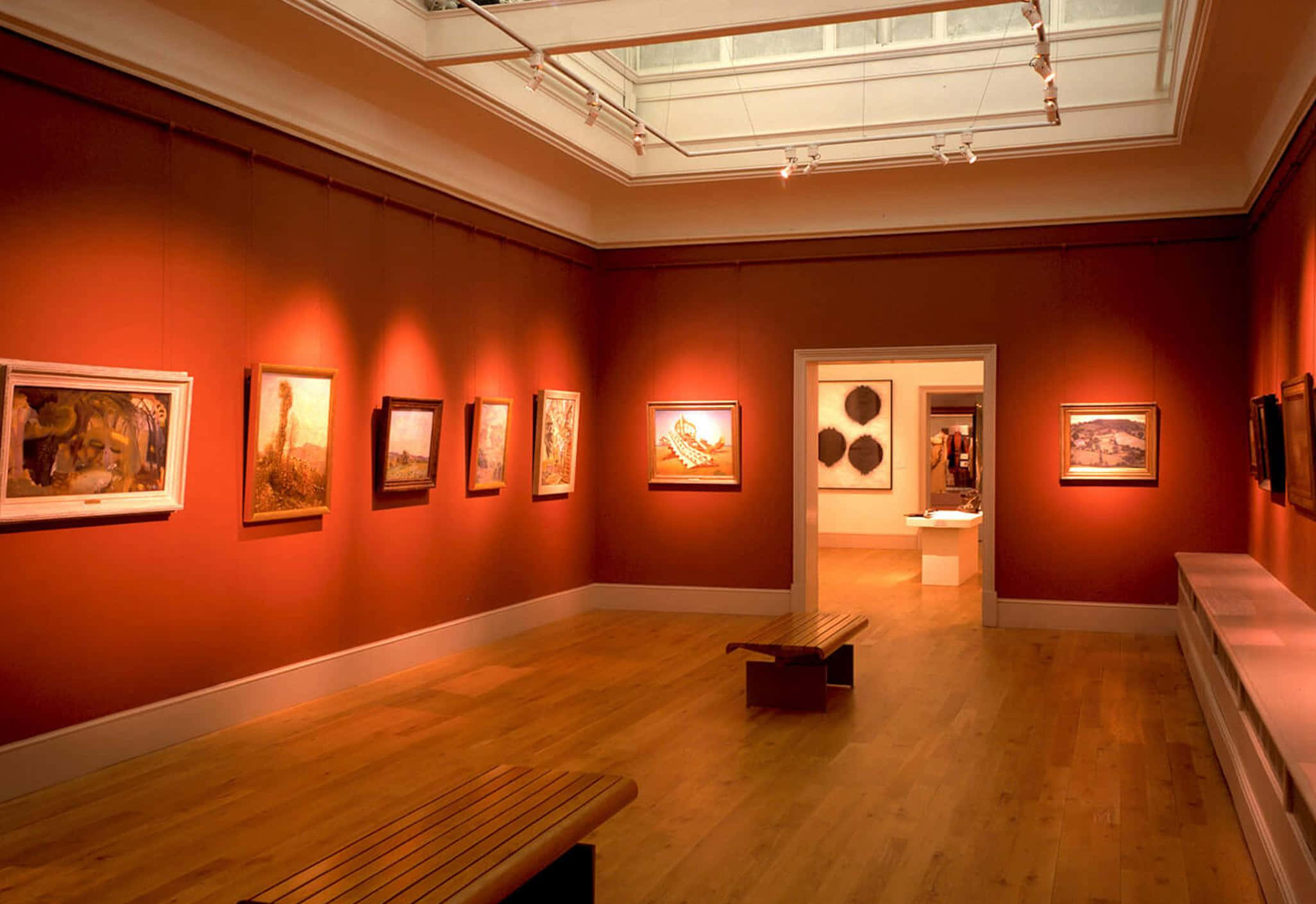 Museum 桌布 壁紙 — 溫暖照明的畫廊，陶土牆壁，在天窗和聚光燈下展示帶框畫作，配有木製長凳。