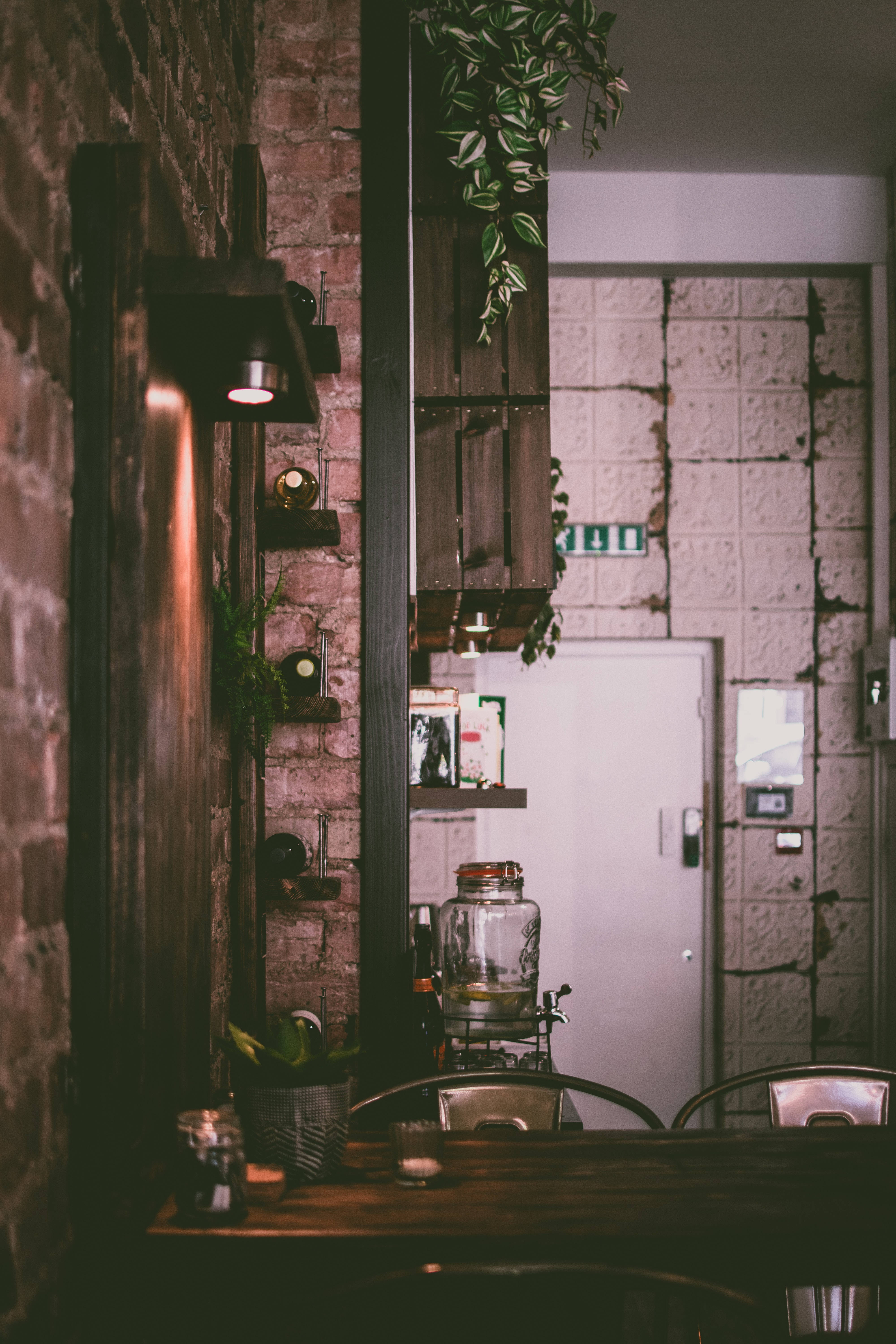 Home 桌布 壁紙 — 溫暖照明的鄉村風格咖啡館內部，裸露磚牆、懸掛綠植和復古裝飾。