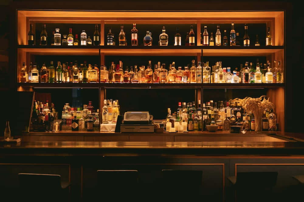 Bar 桌布 壁紙 — 溫暖照明的酒吧架上，在黑暗背景下展示一排排發光的酒瓶。