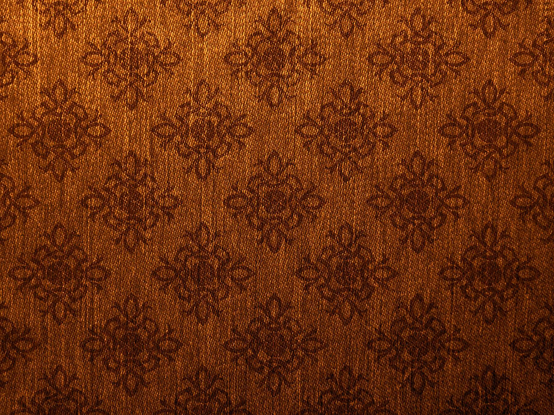 Old Paper 桌布 壁紙 — 溫暖燈光下，帶有重複花卉刺繡圖案的濃郁棕色布料的特寫。