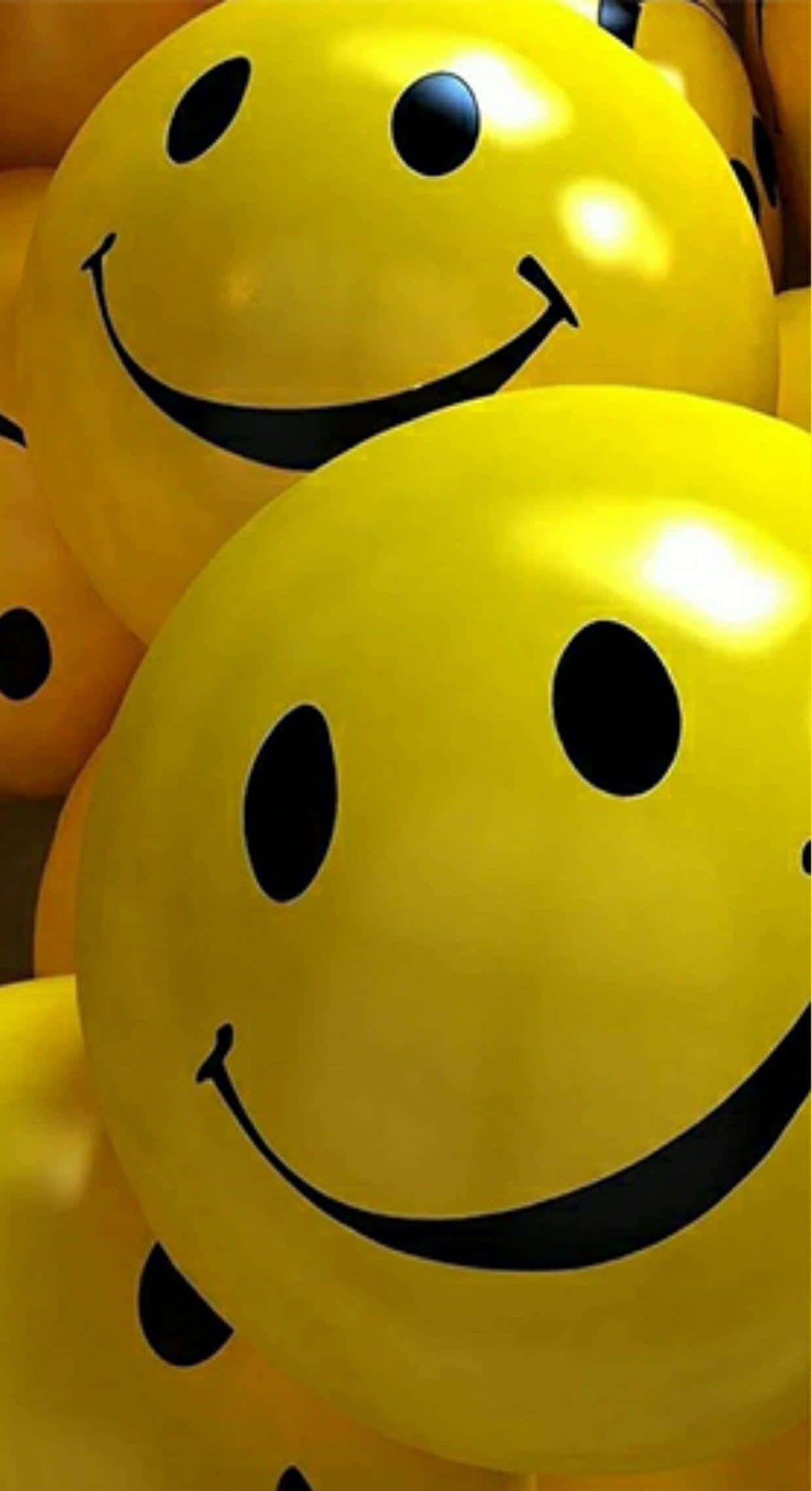 iPhone Emoji 桌布 壁紙 — 溫暖燈光下，明亮黃色氣球的特寫，帶有醒目黑色笑臉圖案，散發光芒。