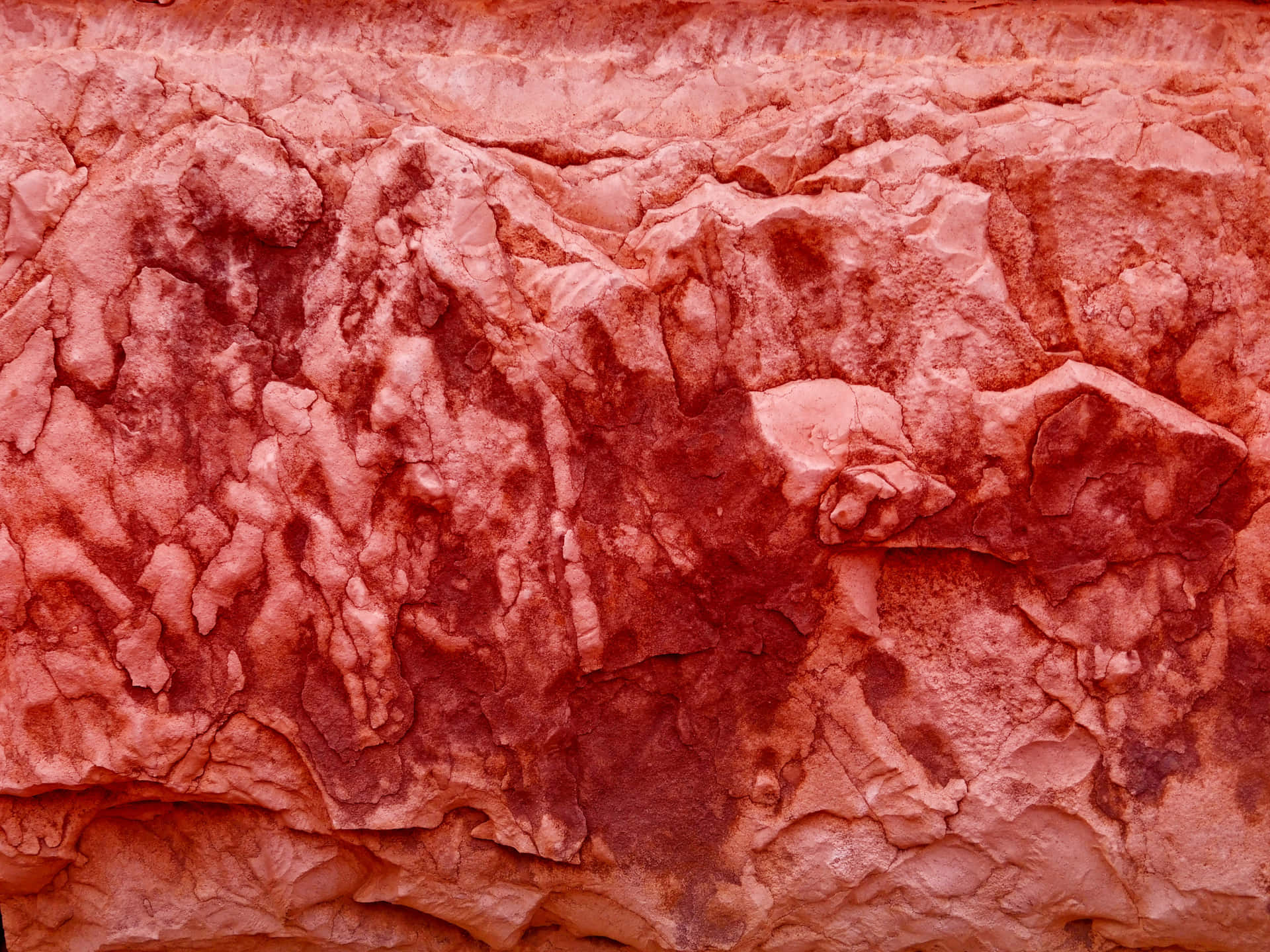 Red stone texture 壁紙 — 溫暖燈光下，粗糙紅色岩層的近距離特寫，具有層狀紋理和深裂縫。
