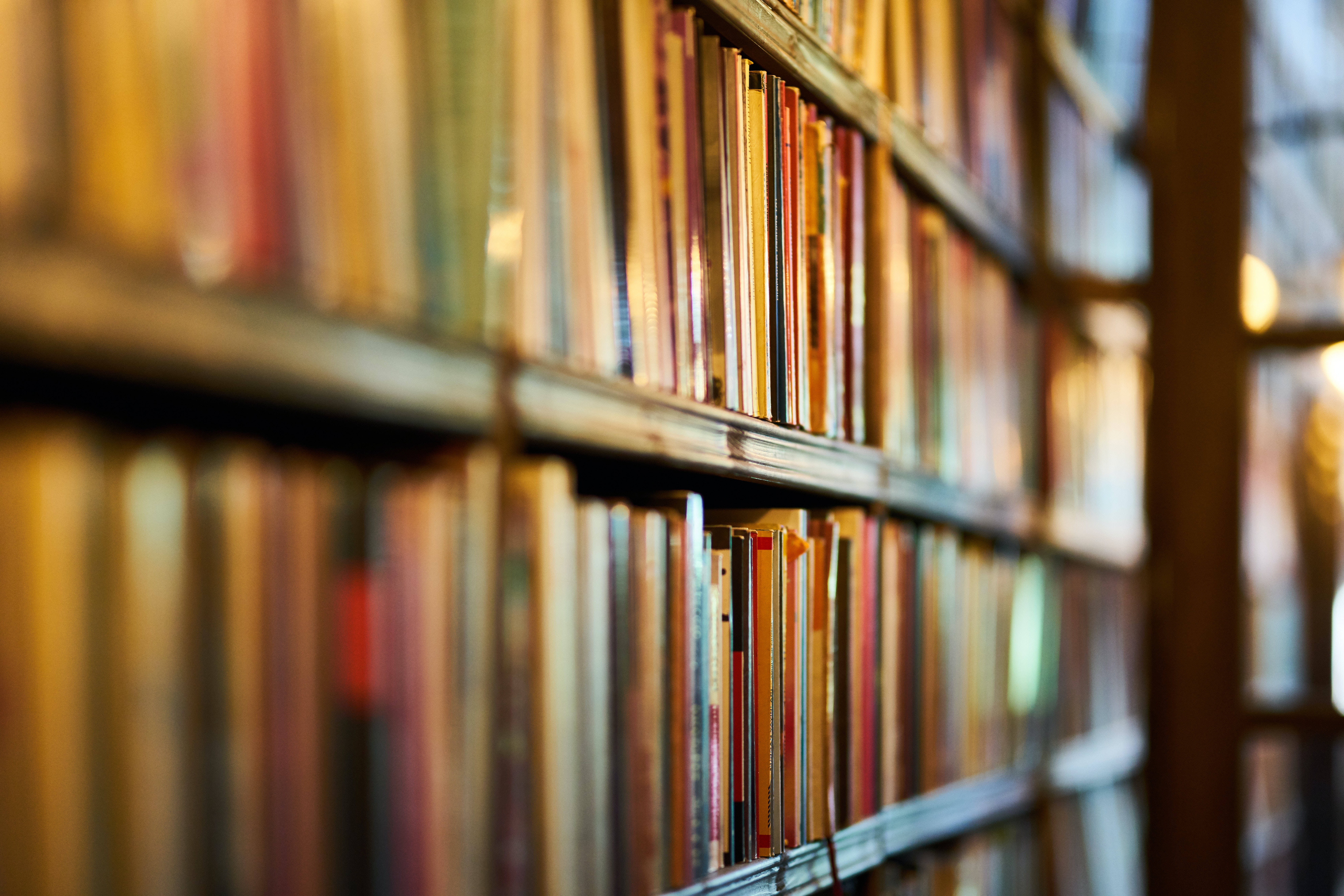 Library 桌布 壁紙 — 溫暖燈光照亮的書架上擺滿了色彩繽紛的書脊，營造出舒適的知識氛圍。