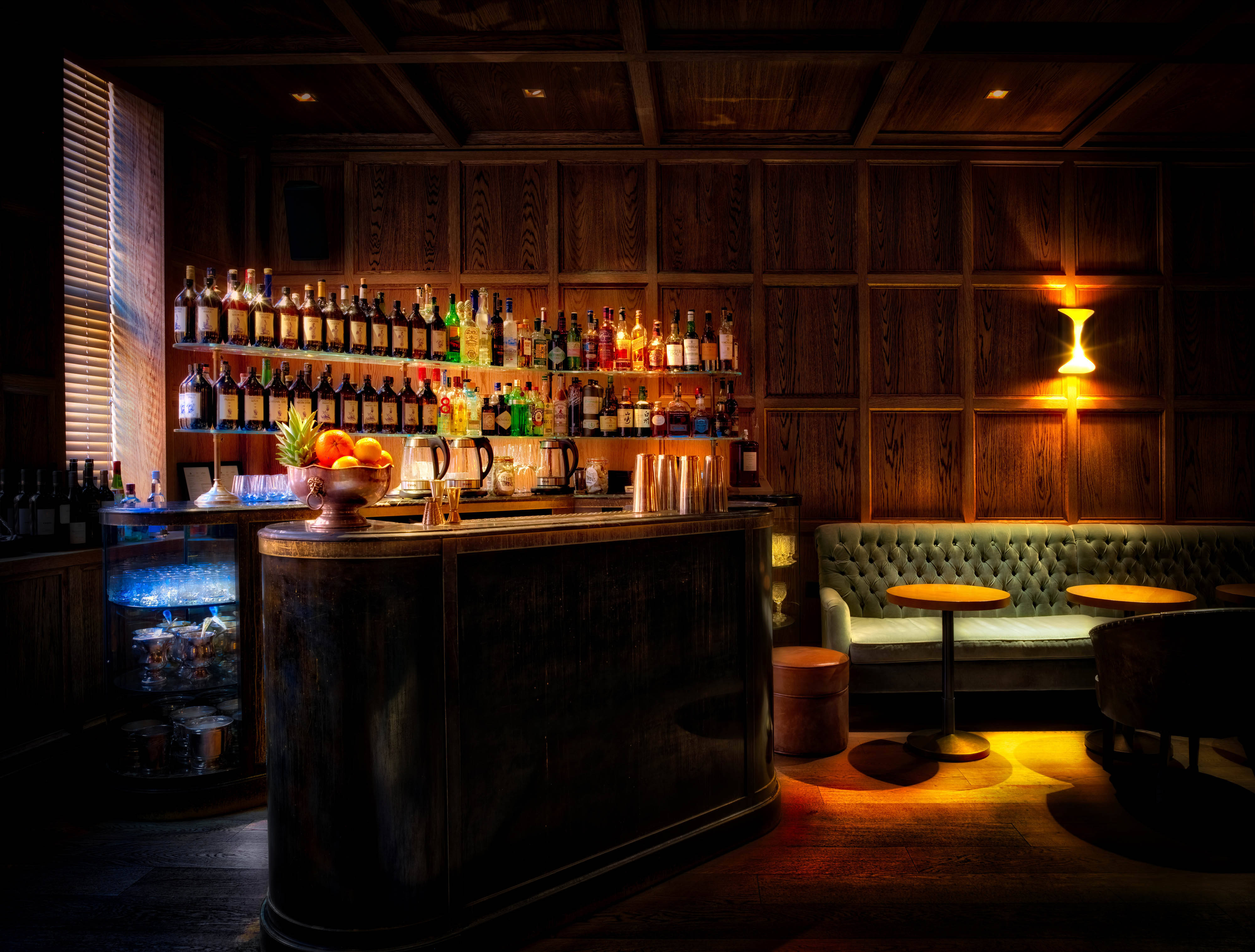 Bar 桌布 壁紙 — 溫暖燈光的復古酒吧，配有木鑲板、擺滿酒類的貨架，以及沐浴在金色光線中的豪華綠色座椅。