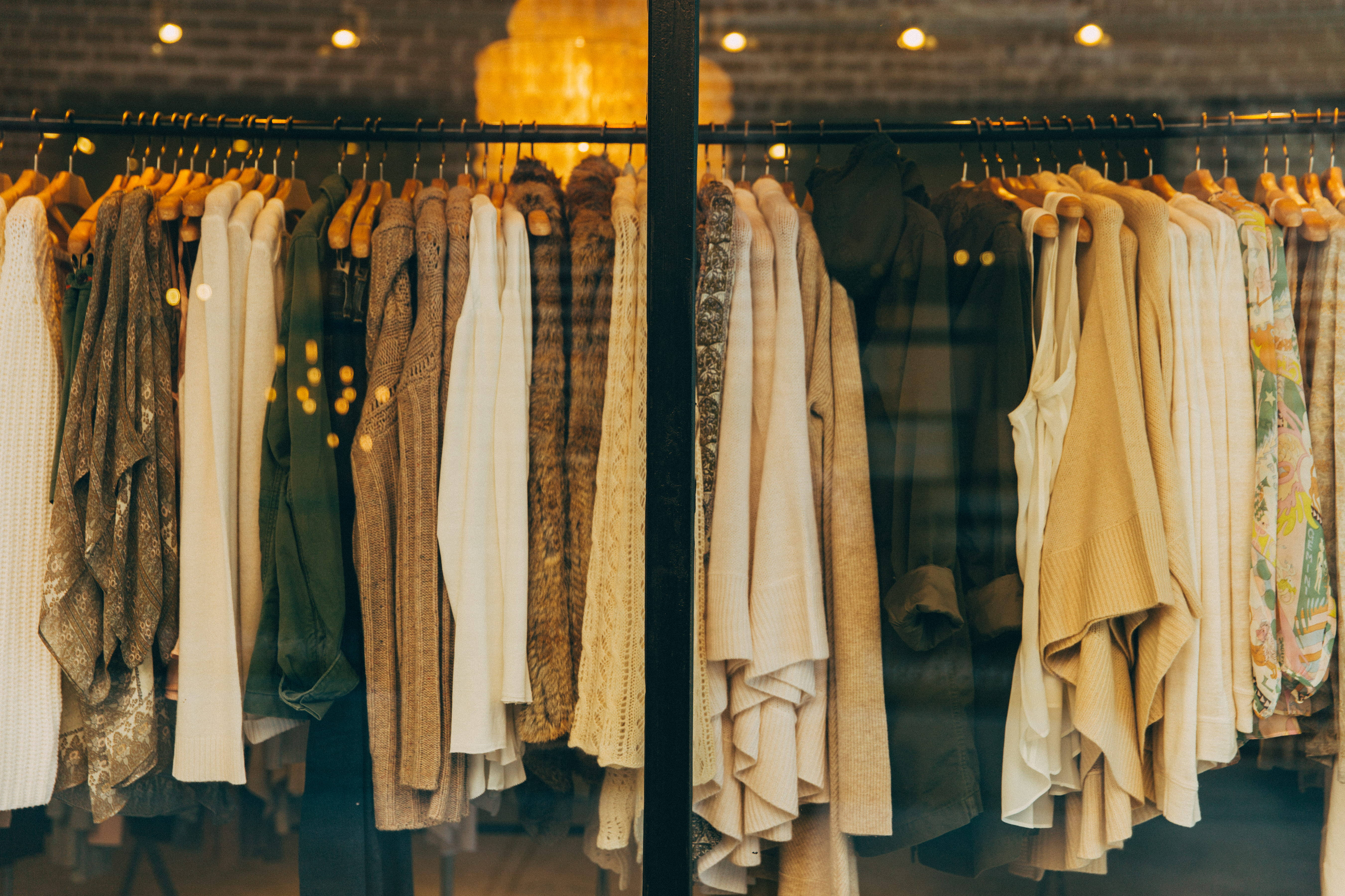 Clothes 桌布 壁紙 — 溫暖燈光的精品店櫥窗展示一排排大地色調的衣物掛在木衣架上，背景是磚牆。