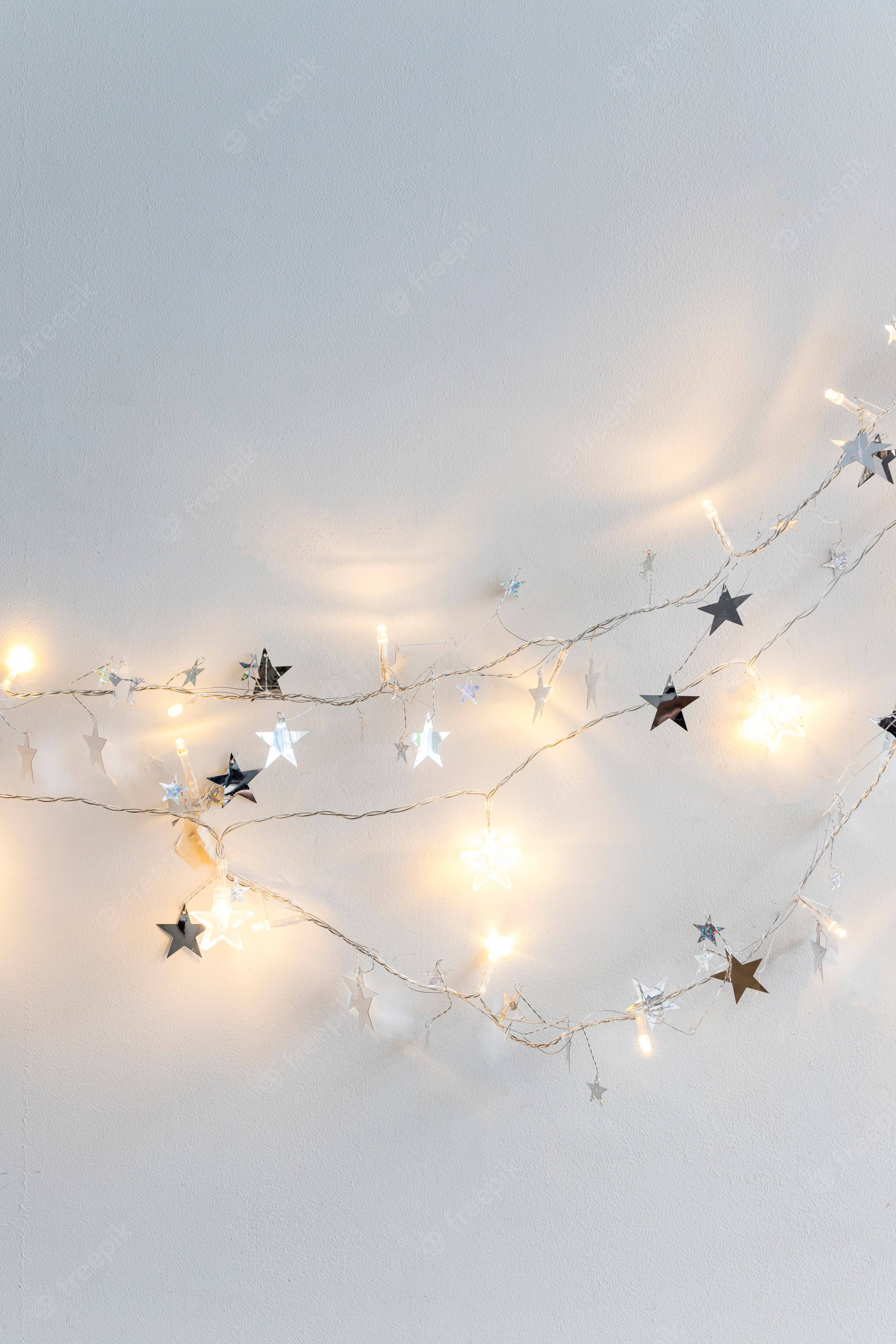 Fairy Lights Aesthetic 桌布 壁紙 — 溫暖發光的星形串燈斜掛在柔軟有紋理的白色牆壁上。