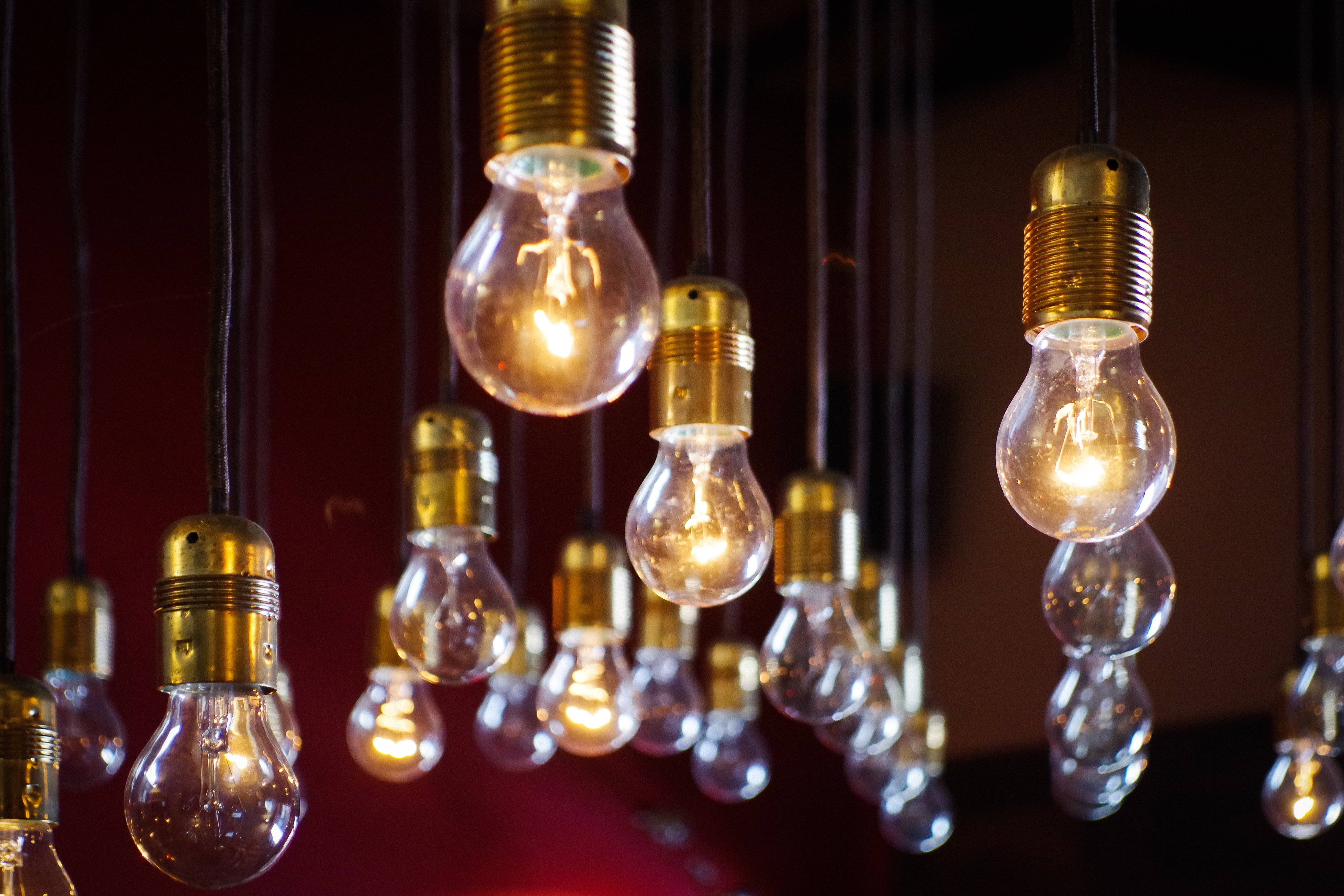 Light Bulb 桌布 壁紙 — 溫暖發光的燈泡懸掛在黑暗的房間中，在深紅色背景下投射出柔和的金色光芒。