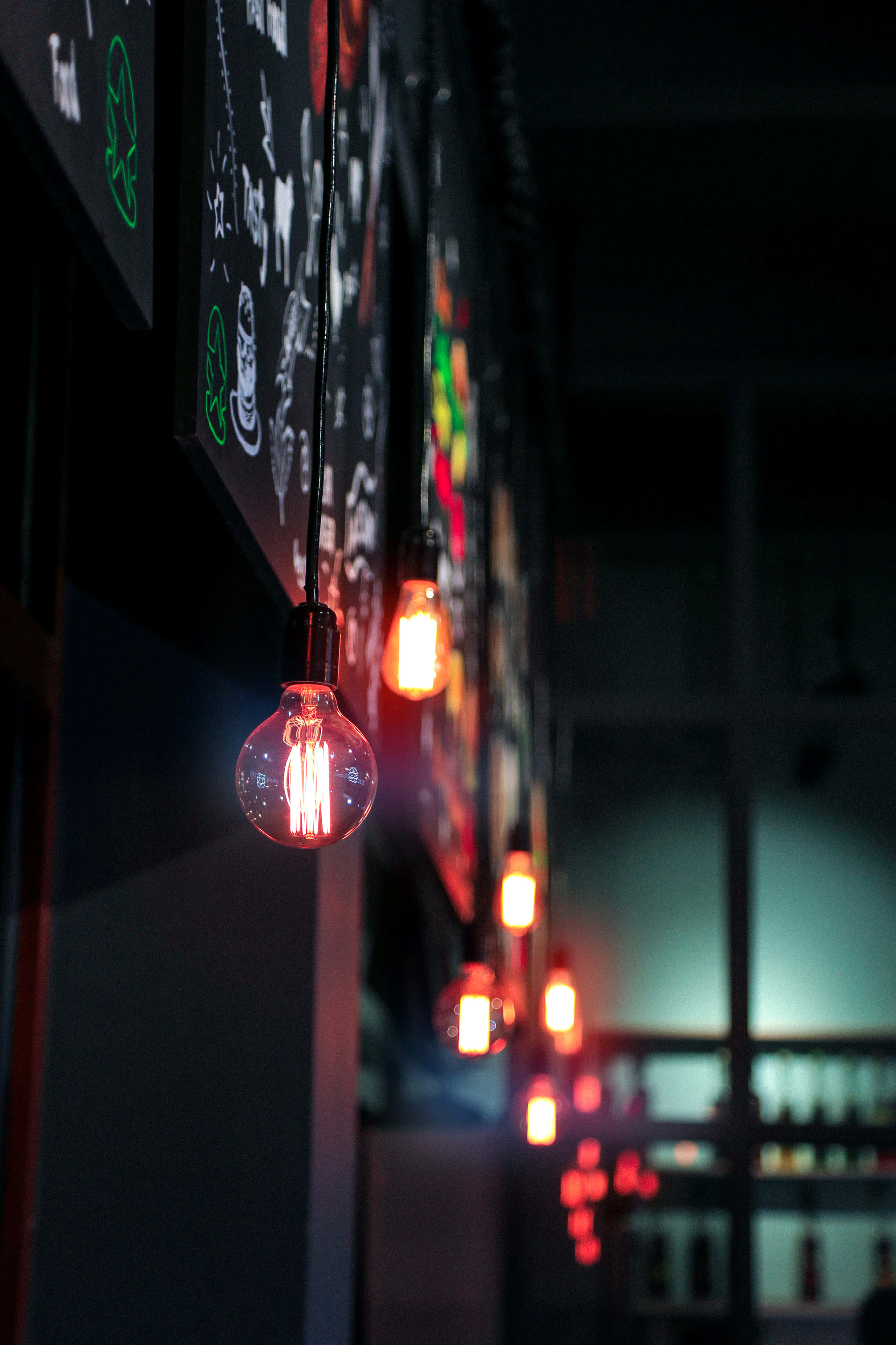 lighting 桌布 壁紙 — 溫暖發光的燈泡排成一排，掛在深色牆壁上，搭配色彩繽紛的粉筆板藝術，營造出舒適昏暗的咖啡館氛圍。