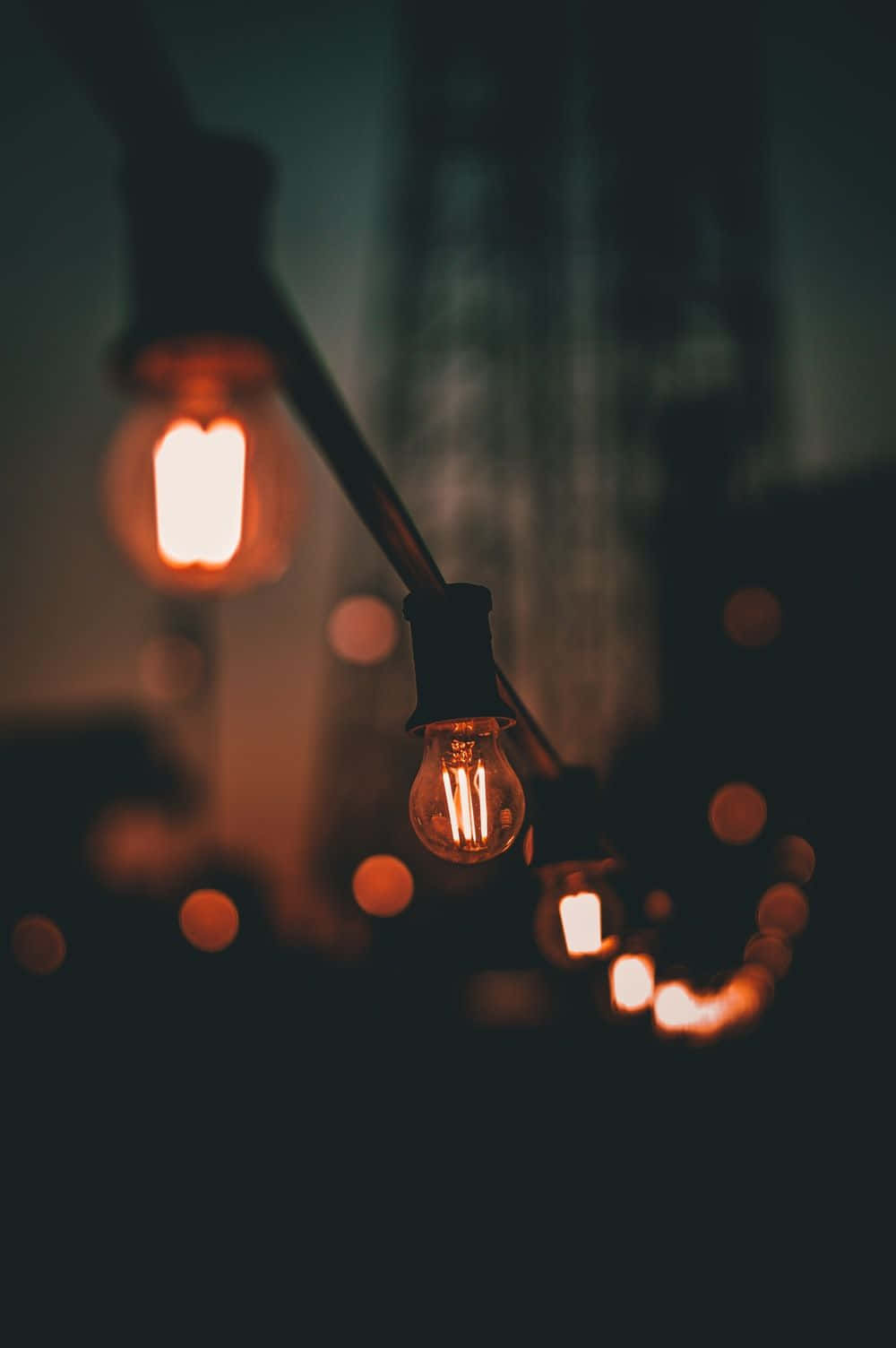 Light Effect 桌布 壁紙 — 溫暖發光的燈絲燈泡掛在一條繩子上，背景是黑暗模糊的，營造出舒適親密的氛圍。