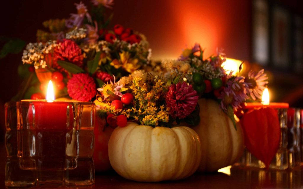Thanksgiving Day 桌布 壁紙 — 溫暖發光的蠟燭兩旁襯托著一個質樸的南瓜中心裝飾，綴滿了秋季的花朵和漿果。