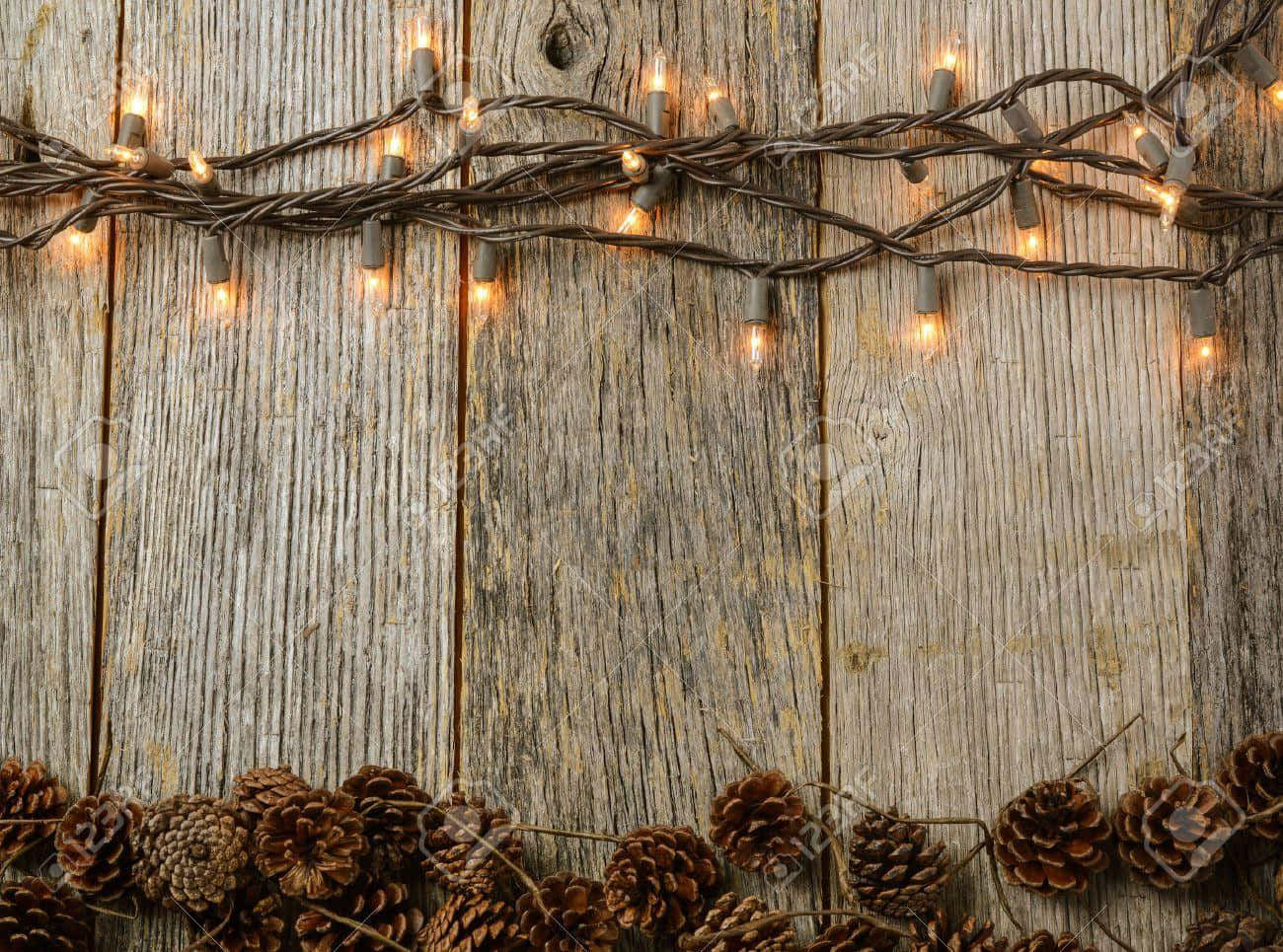 Rustic Christmas 桌布 壁紙 — 溫暖的串燈在風化的木板上閃爍，底部有一排松果。