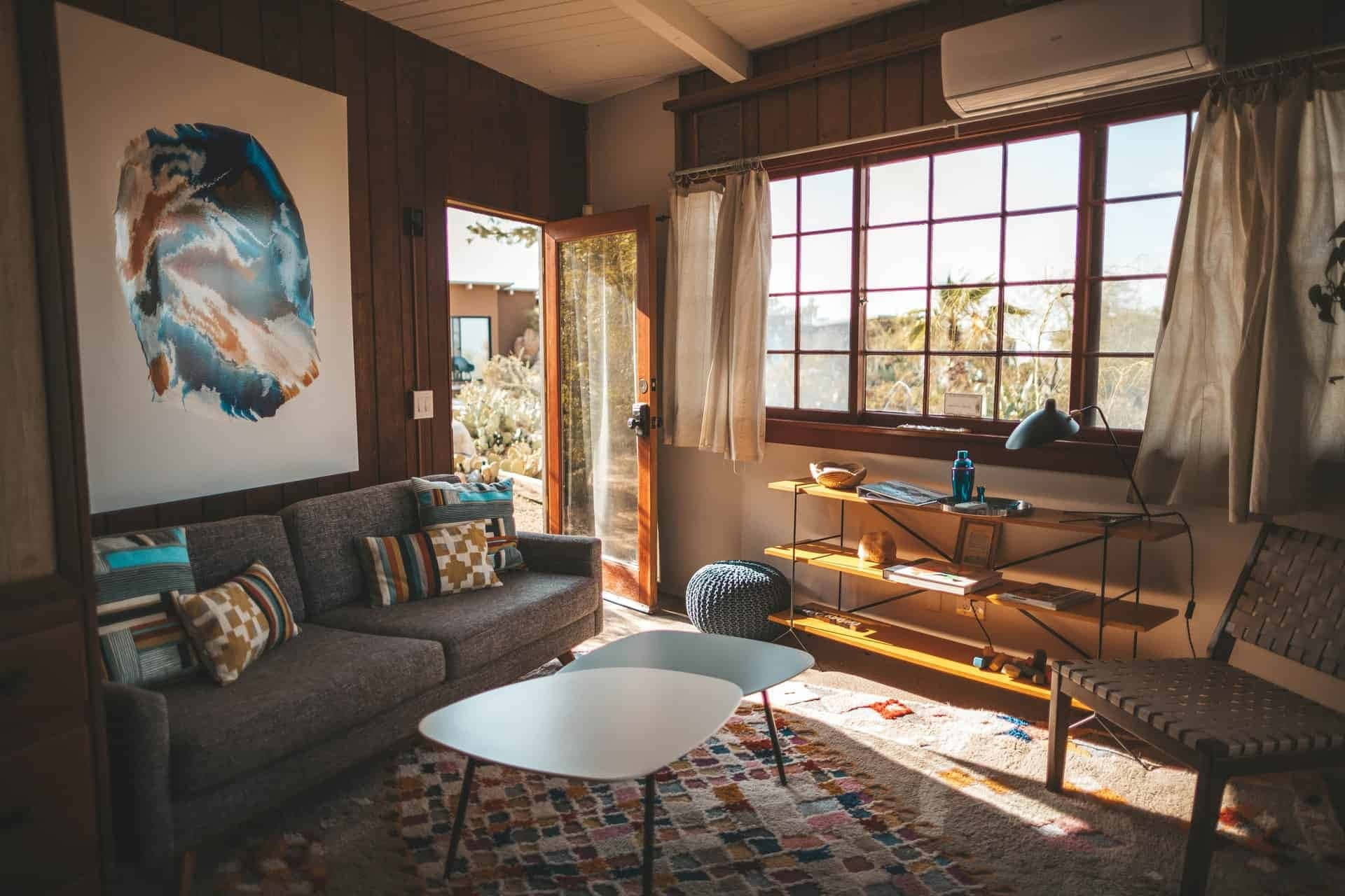 Living Room 桌布 壁紙 — 溫暖的木質室內，金色陽光透過大窗戶灑在圖案地毯和現代家具上。