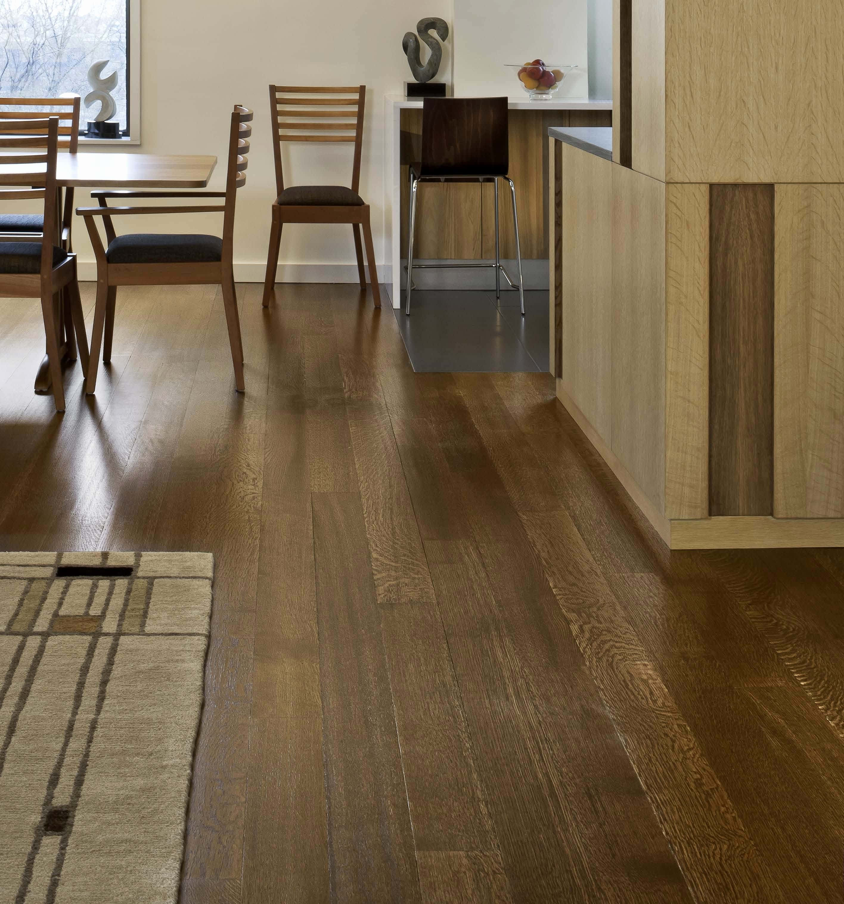 Wood Floor 桌布 壁紙 — 溫暖的硬木地板延伸穿過現代用餐區，配有木椅和圖案地毯，在柔和自然光下。