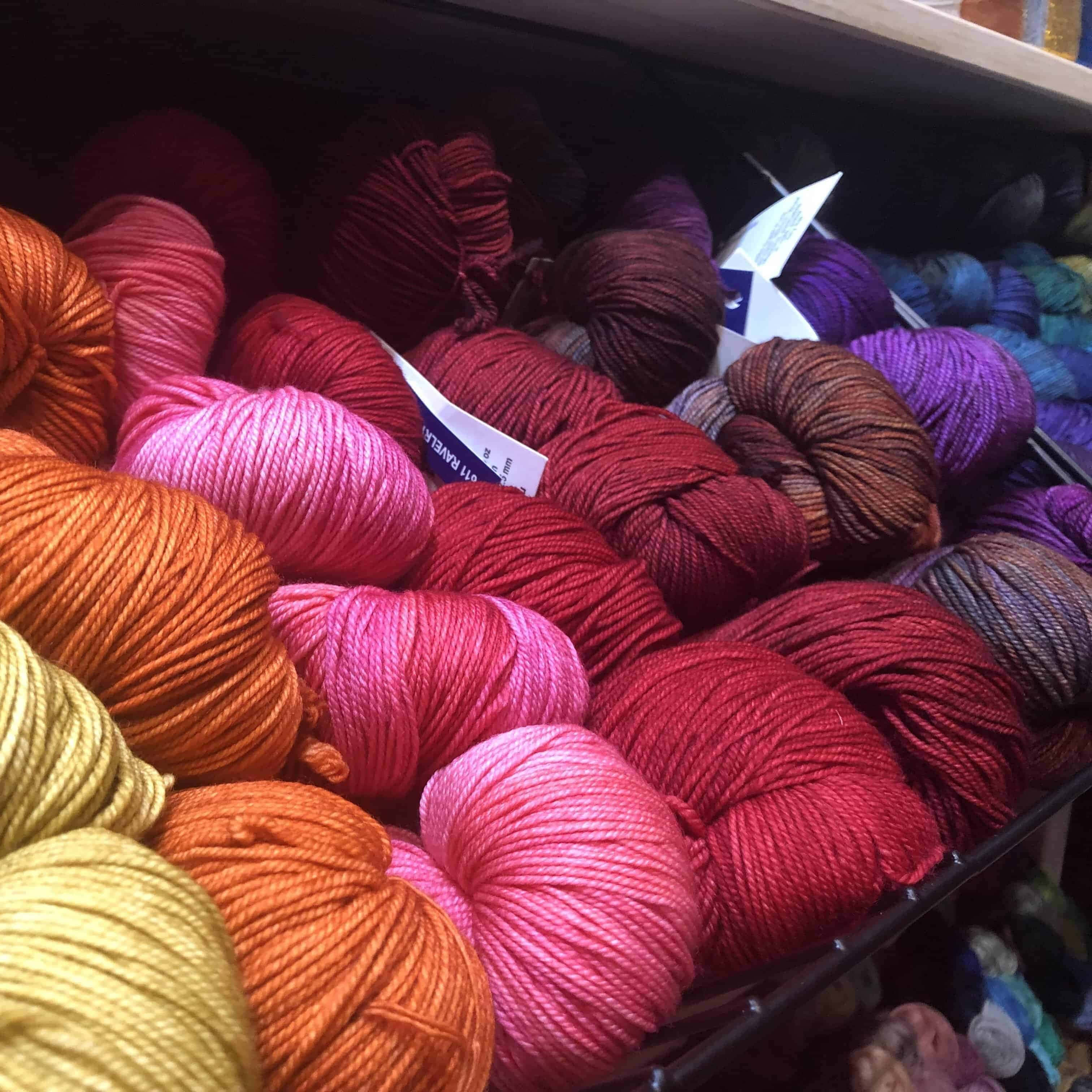 Knitting 桌布 壁紙 — 溫暖的紅色、粉紅色、橙色和紫色鮮豔毛線球緊密堆疊在架子上。