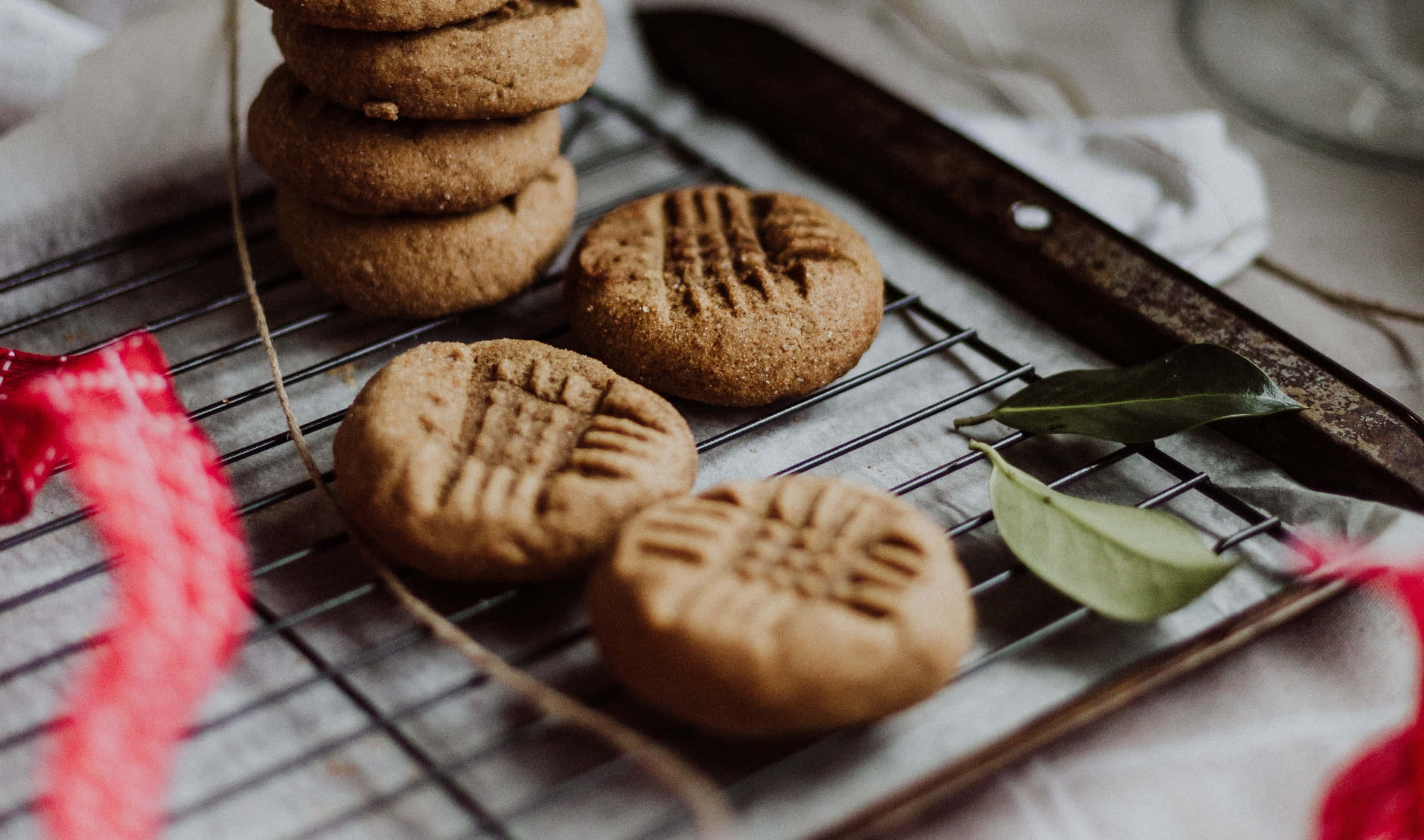 Cookies 桌布 壁紙 — 溫暖的花生醬餅乾，帶有經典的交叉花紋，放在金屬架上，旁邊有一把鄉村風格的刀和綠葉。