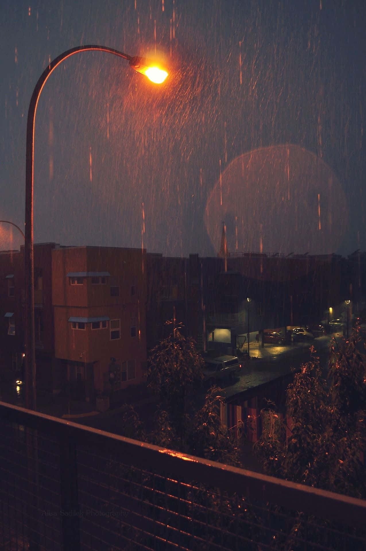 Rainy Day 桌布 壁紙 — 溫暖的街燈在漆黑的雨夜中發出琥珀色的光芒，照亮了落下的雨滴和濕漉漉的城市建築。
