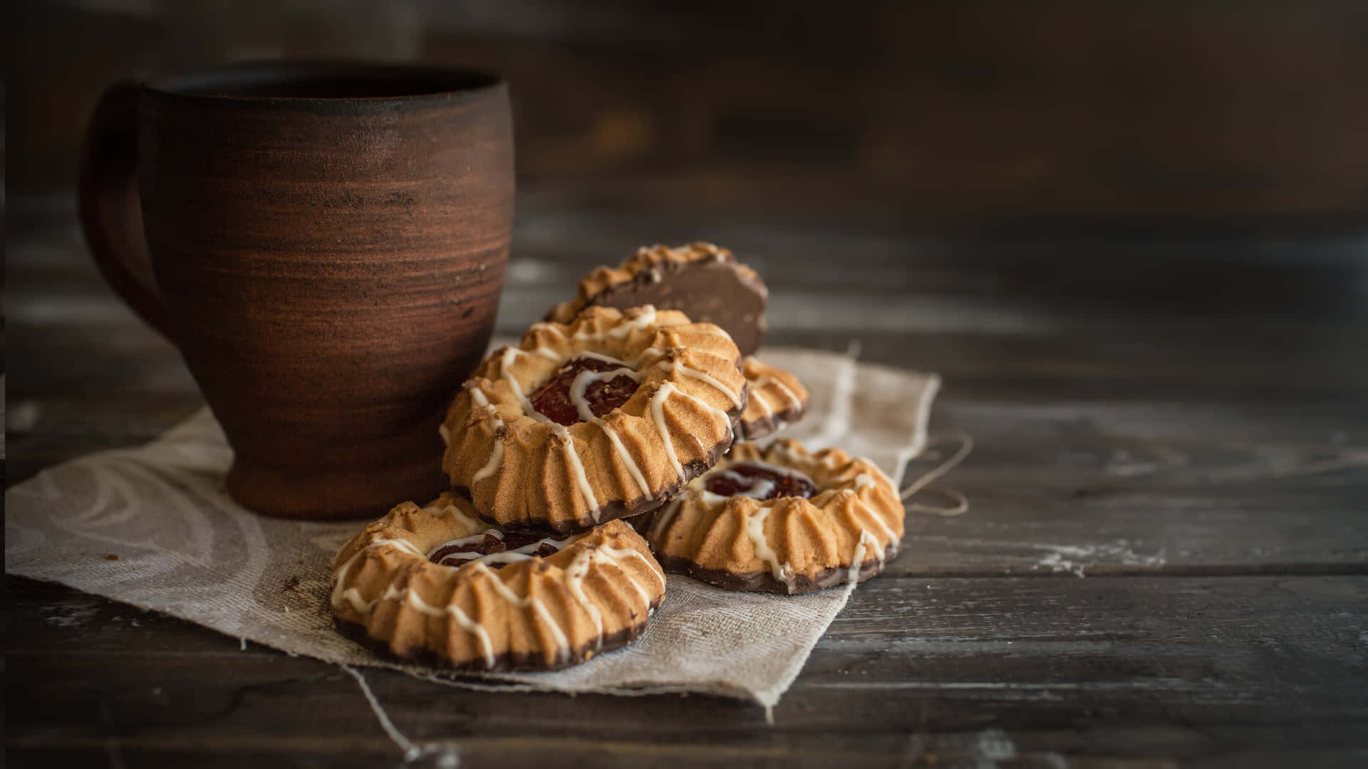 Pastry 桌布 壁紙 — 溫暖的鄉村風格餅乾，中間有果醬和白色糖霜，旁邊放著一個陶瓷杯在木桌上。