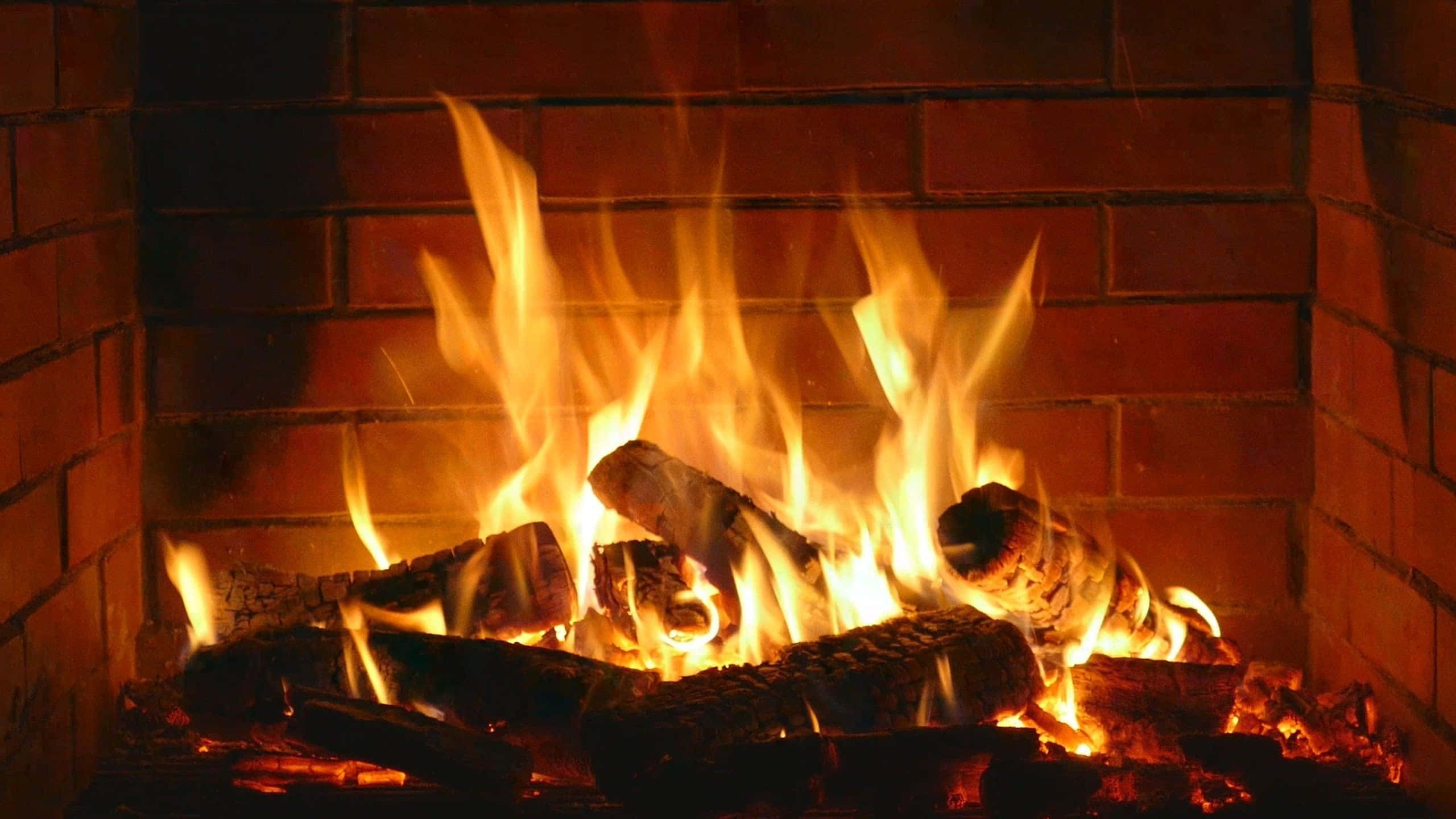 Cozy Fire 桌布 壁紙 — 溫暖的金色火焰從鄉村磚砌壁爐中劈啪作響的木柴上躍起，在周圍的磚塊上投下柔和的光線。