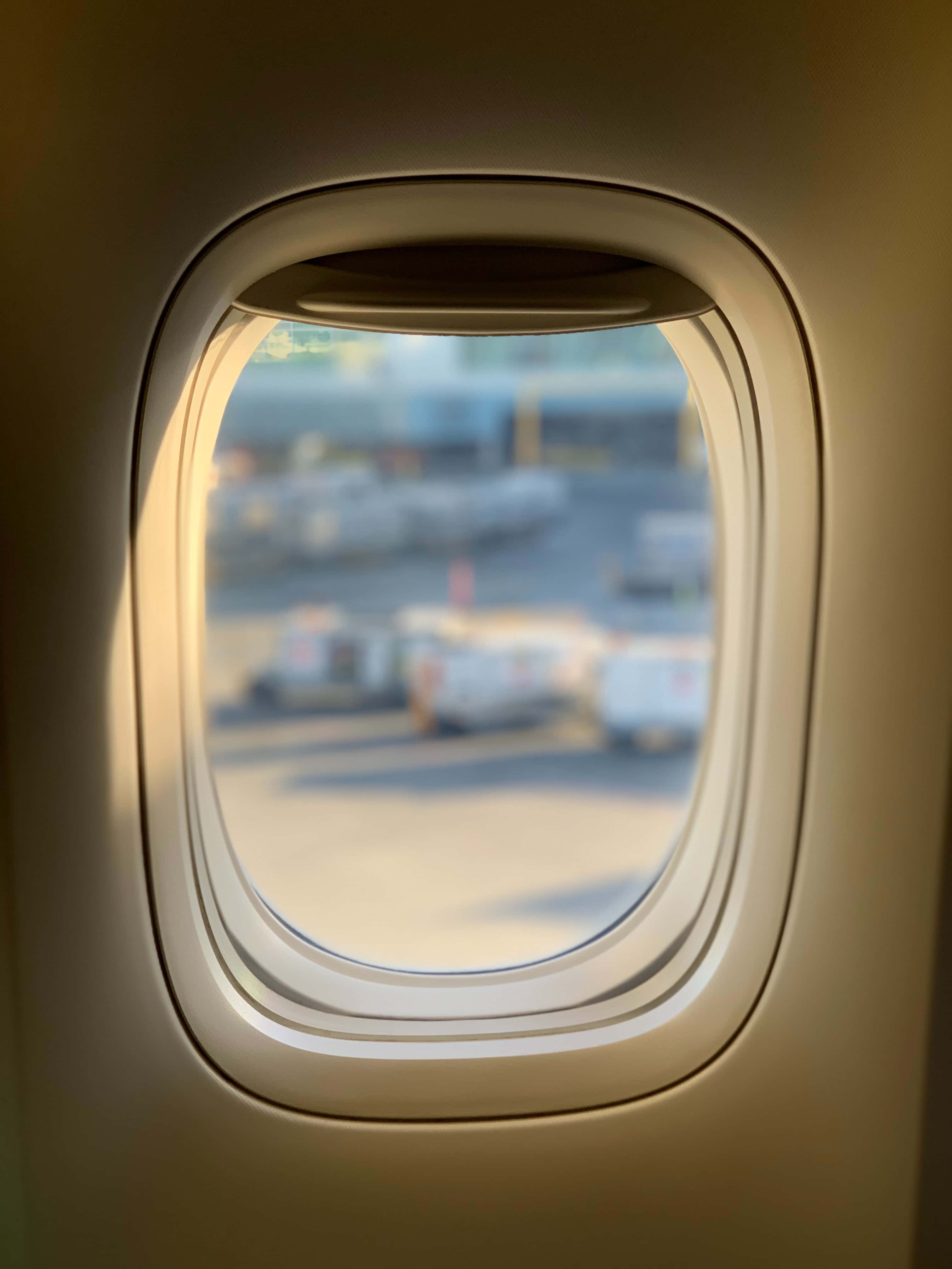 window 桌布 壁紙 — 溫暖的陽光透過飛機窗戶照射進來，顯現出模糊的機場停機坪和地面車輛。