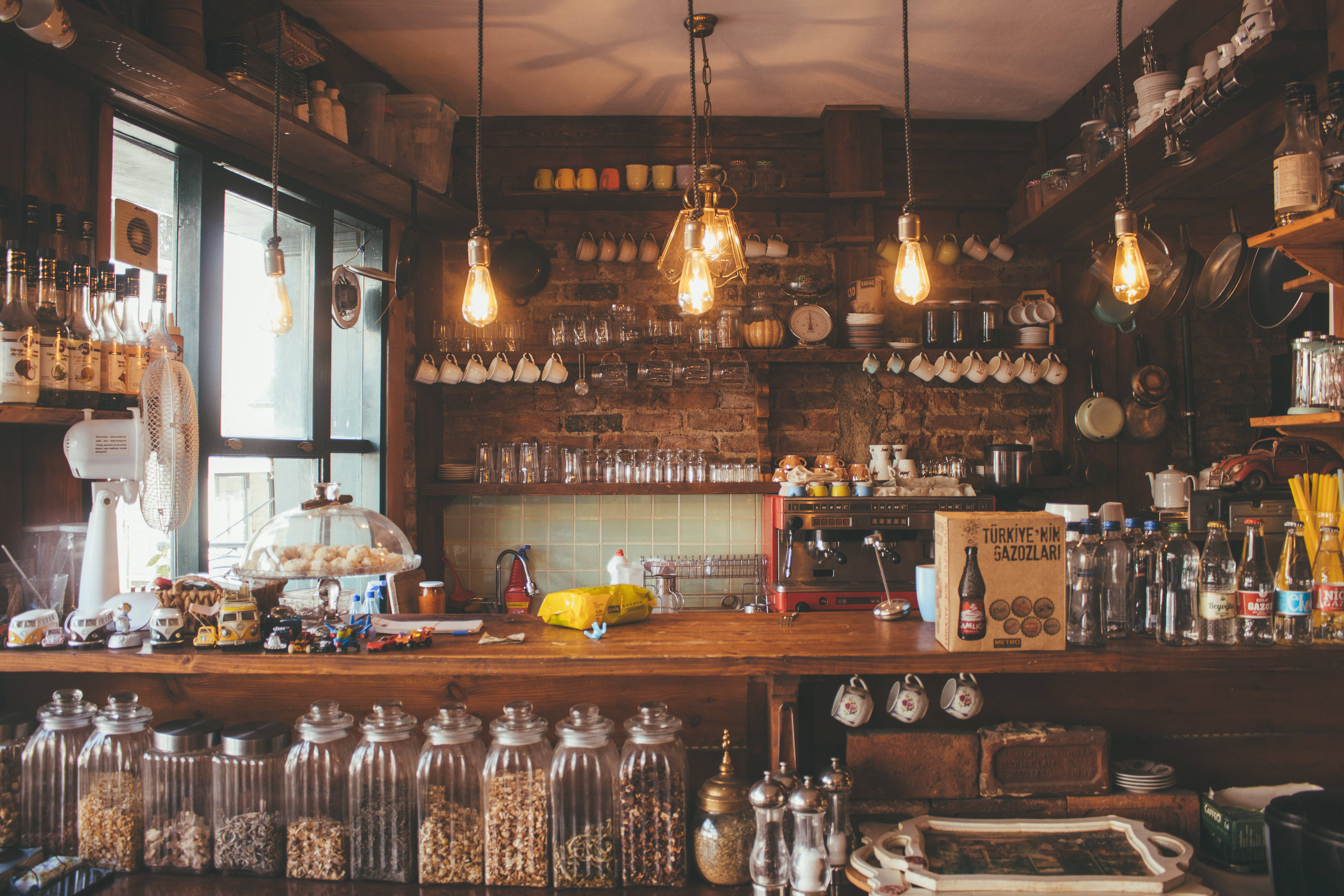 Coffee Shop 桌布 壁紙 — 溫暖質樸的咖啡館內部，設有木製櫃檯、玻璃罐、吊燈和充滿復古廚具的磚牆。