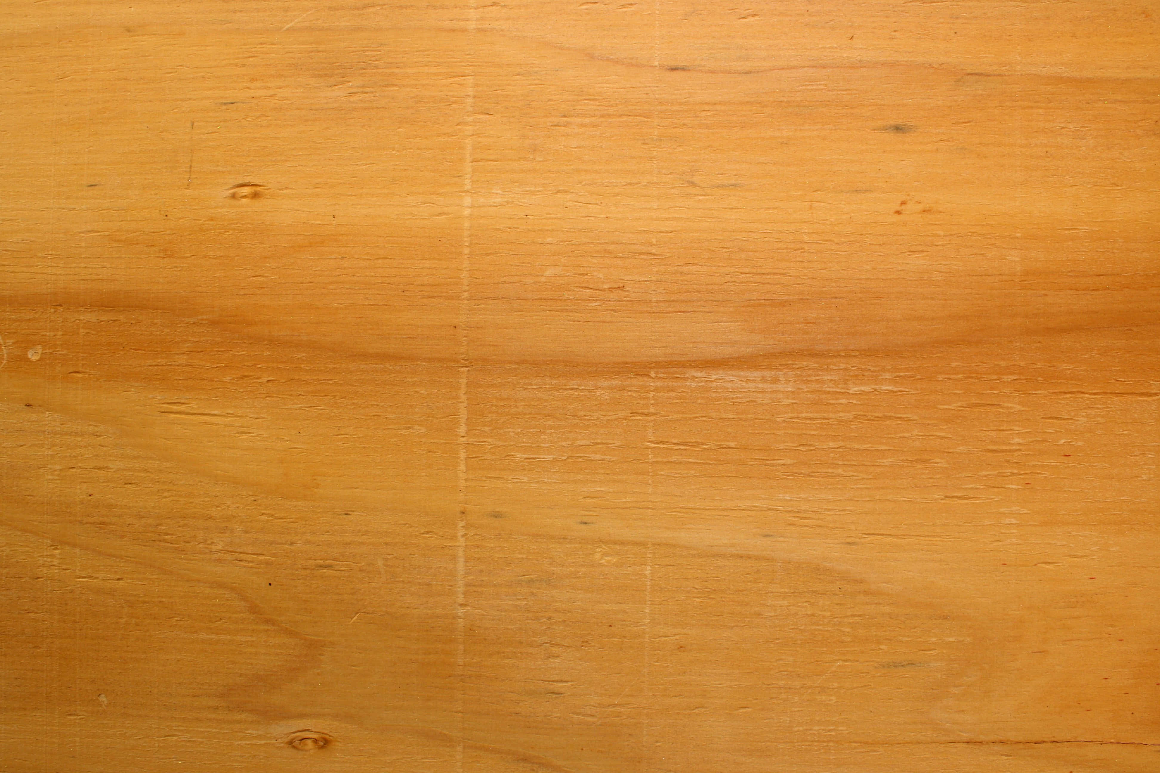 Wood Texture 桌布 壁紙 — 溫暖金色合板表面的特寫，顯示天然木紋節和細微刮痕。