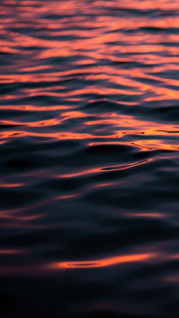 海洋 桌布 壁紙 — 溫柔的波浪在黑暗的水面上蕩漾，反射出夕陽火熱的橙色和紅色色調。