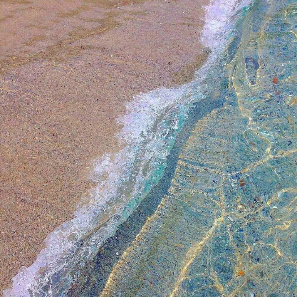 Beach Aesthetic 桌布 壁紙 — 溫柔的海浪沖刷金色沙灘的特寫，在清澈的碧綠海水下顯露出色彩繽紛的鵝卵石。