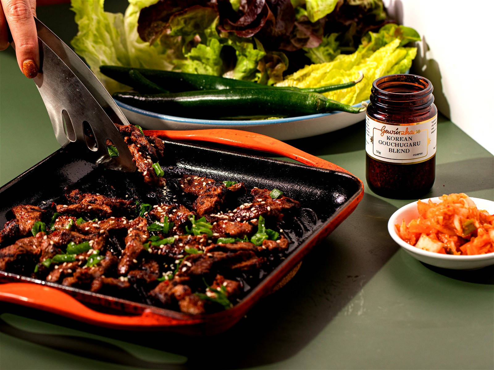Lettuce 桌布 壁紙 — 滋滋作響的韓國牛肉條，飾以芝麻和青蔥，正從熱鍋中撈起，旁邊有新鮮生菜、甜椒和泡菜。