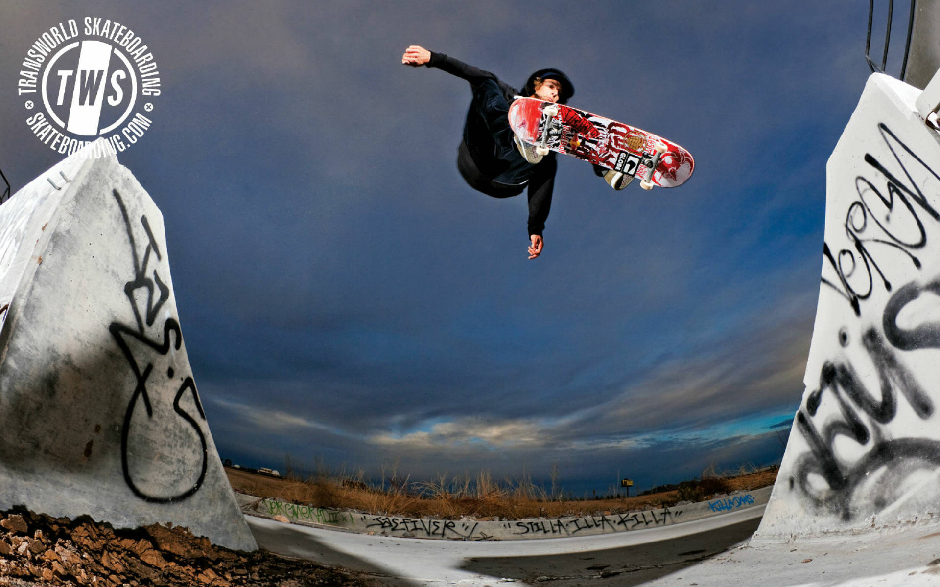 Skater Boy 桌布 壁紙 — 滑板手在半空中，在塗鴉覆蓋的混凝土坡道上表演技巧，背景是戲劇性的黃昏天空。
