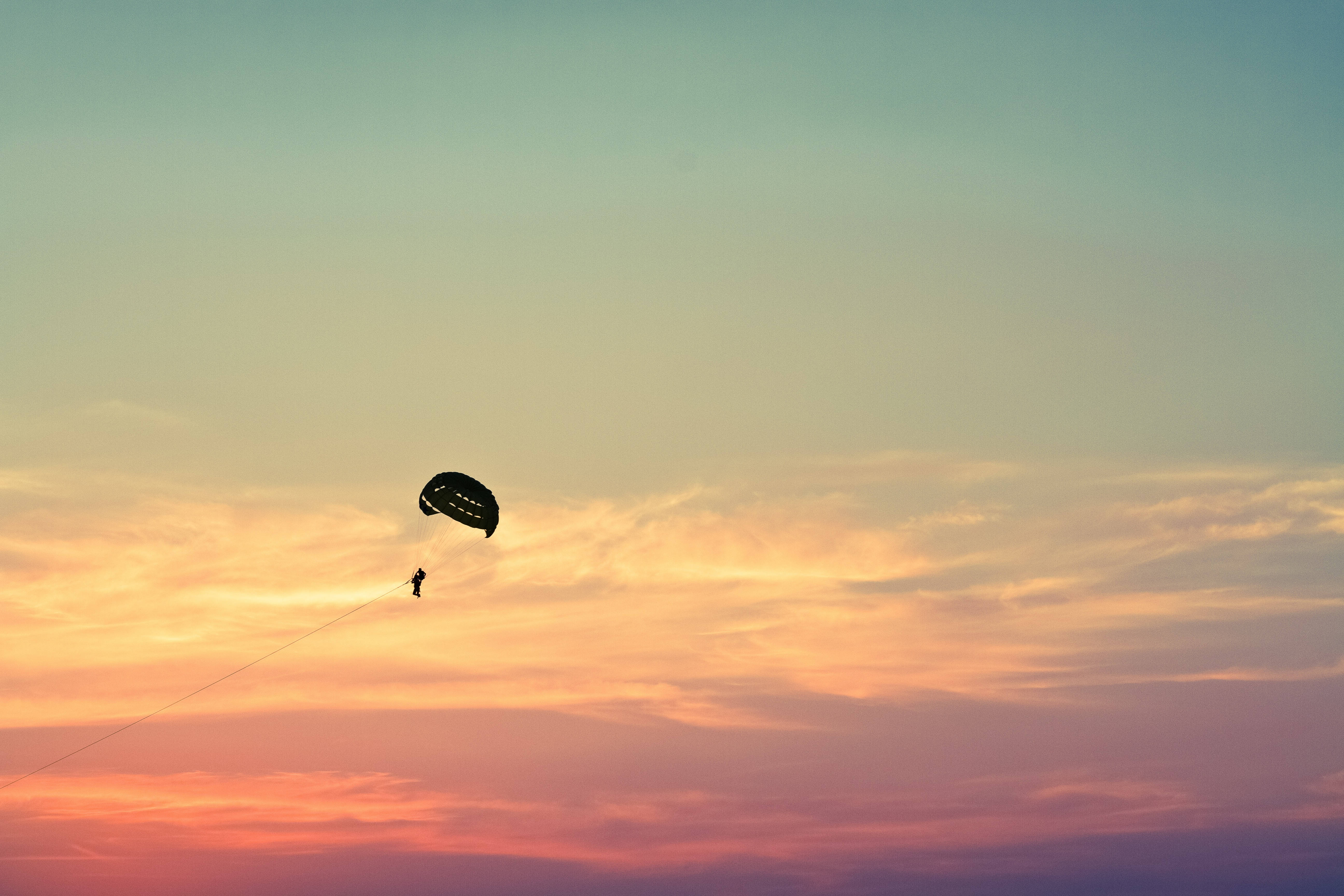 Paragliding 桌布 壁紙 — 滑翔傘剪影映襯著充滿活力的日落天空，帶有橙色、粉紅色和藍綠色的雲彩條紋。