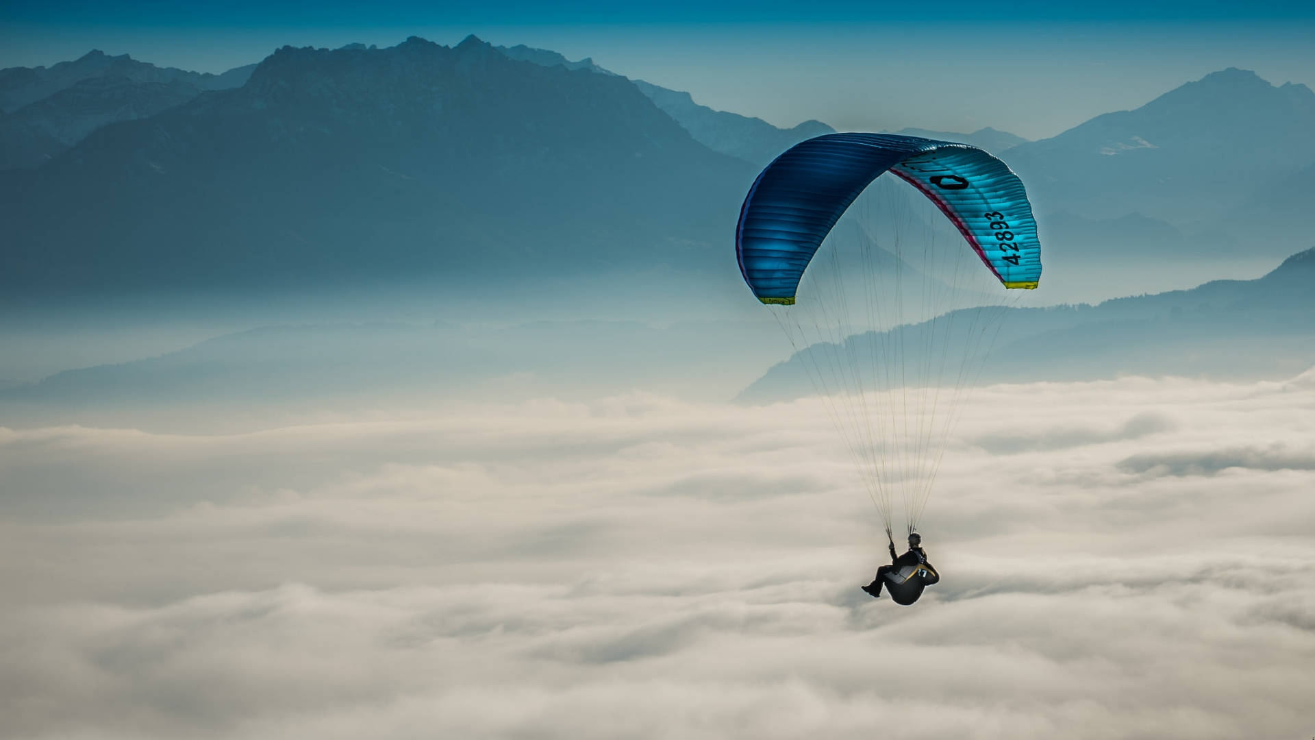 Paragliding 桌布 壁紙 — 滑翔傘在雲海上翱翔，朦朧遠方有雄偉山脈，晴空萬里。