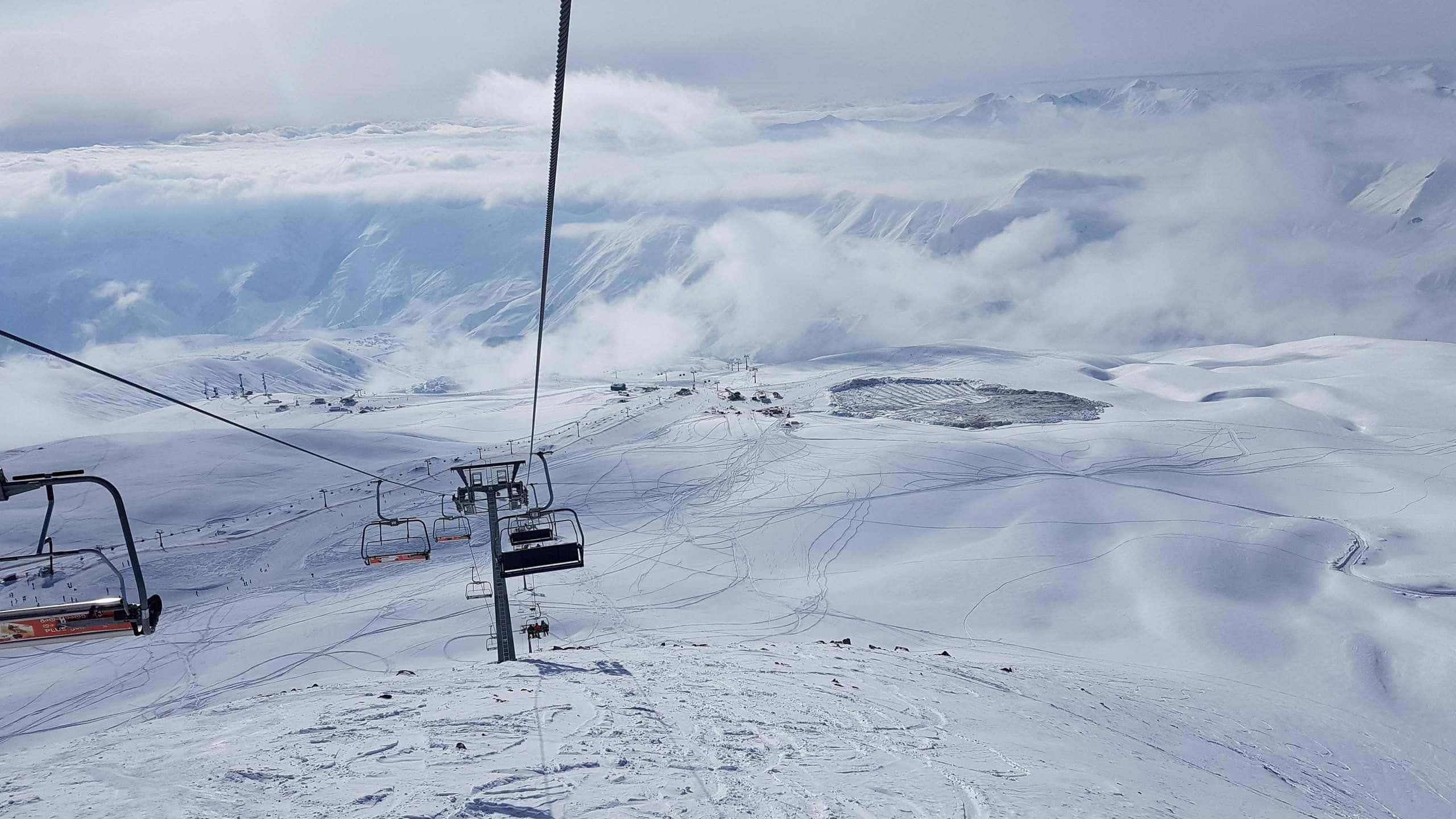 Ski Resort 桌布 壁紙 — 滑雪纜車沿著積雪的山峰上升，俯瞰下方的雲海，滑雪道蜿蜒穿過白色廣闊地帶。