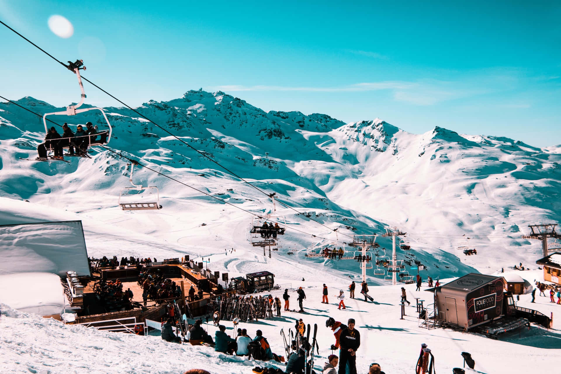 Ski Resort 桌布 壁紙 — 滑雪者和單板滑雪者在陽光明媚的日子裡，在一個繁忙的山區滑雪勝地享受著吊椅和白雪覆蓋的山峰。