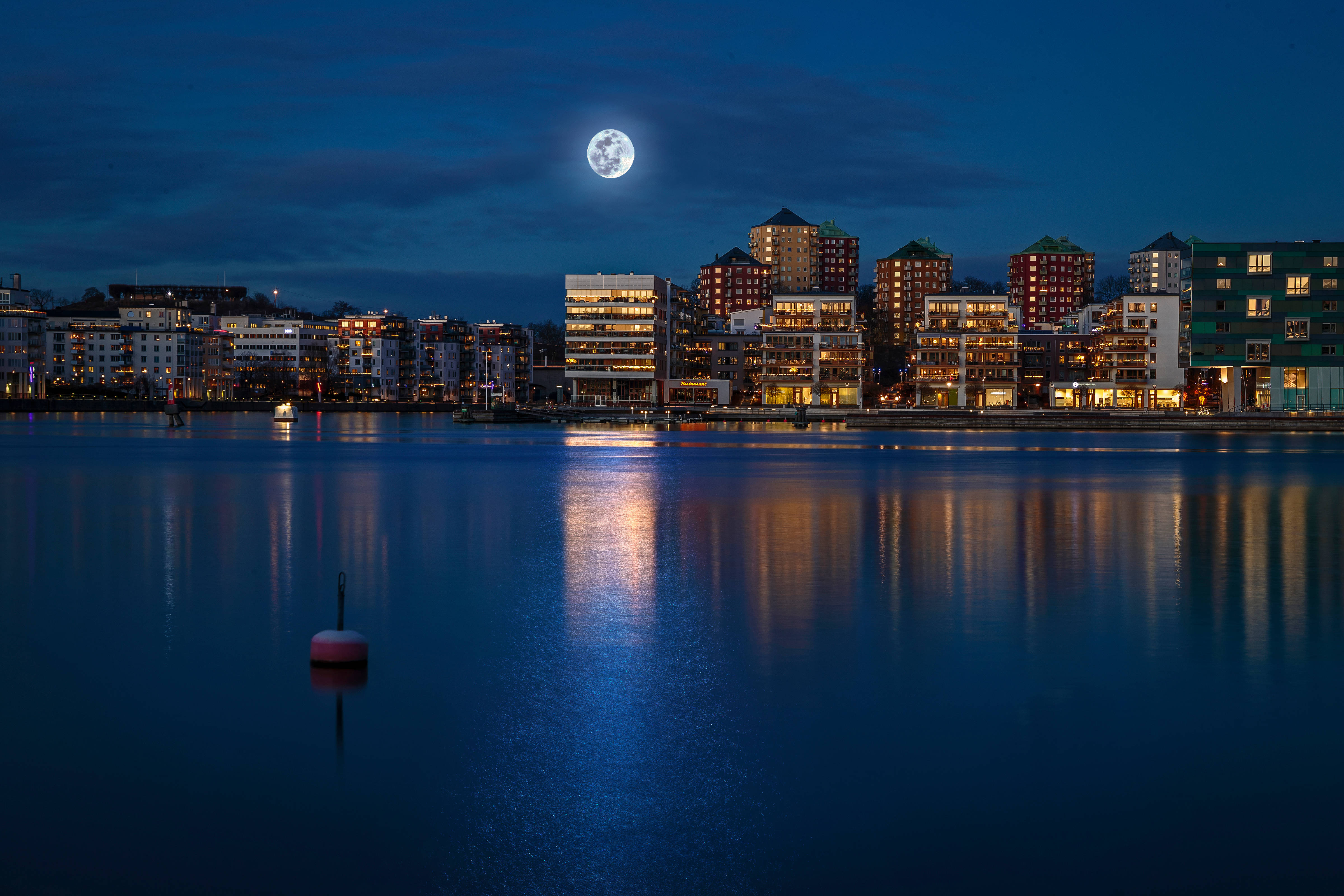 Sweden 桌布 壁紙 — 滿月在寧靜的海濱城市夜景中閃耀，溫暖的燈光倒映在平靜的水面上。