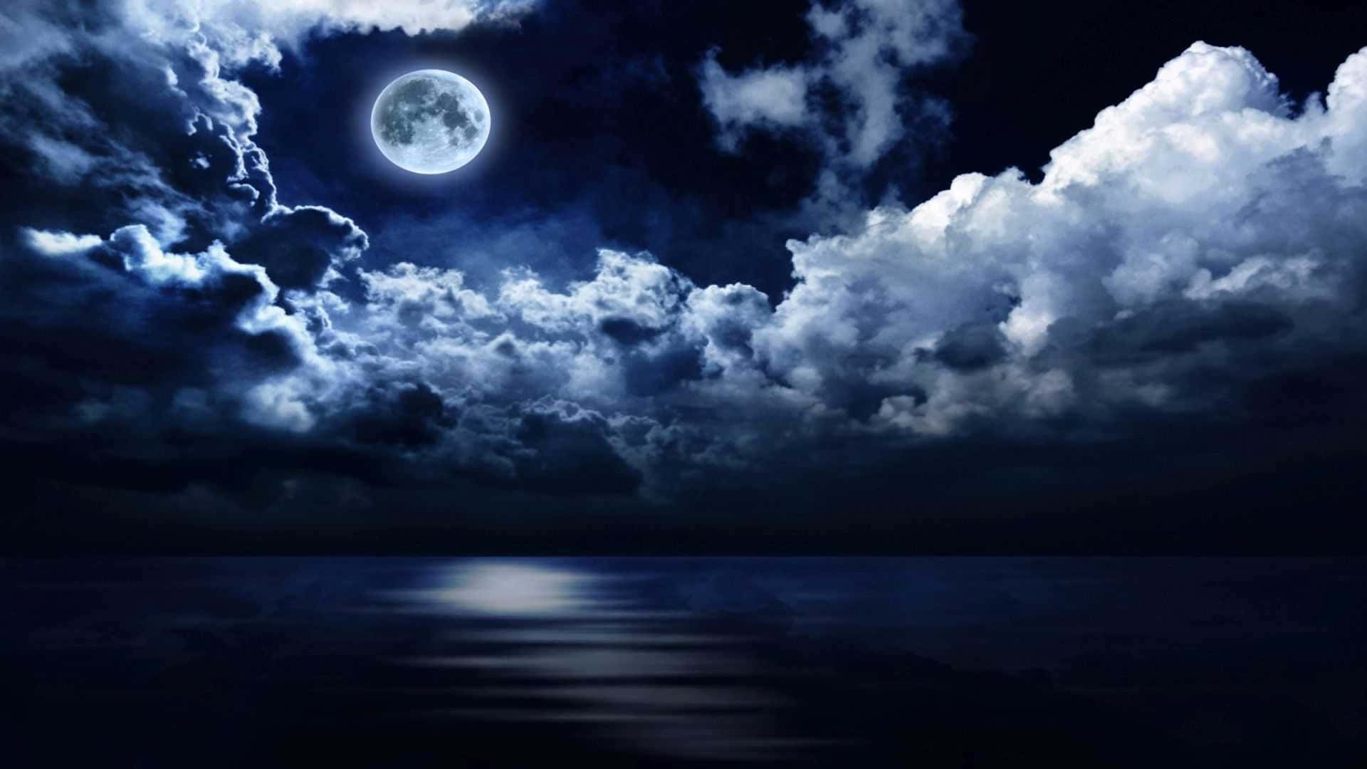 Midnight 桌布 壁紙 — 滿月在戲劇性的雲層中發光，在深藍色夜空下平靜的海洋上投射出一條閃爍的路徑。