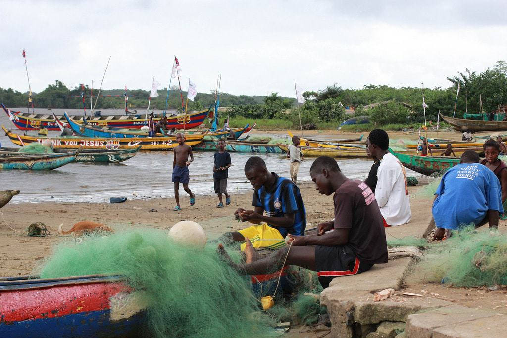 Liberia 桌布 壁紙 — 漁夫在陰天的沙灘上，在色彩繽紛的船隻旁邊修補漁網。