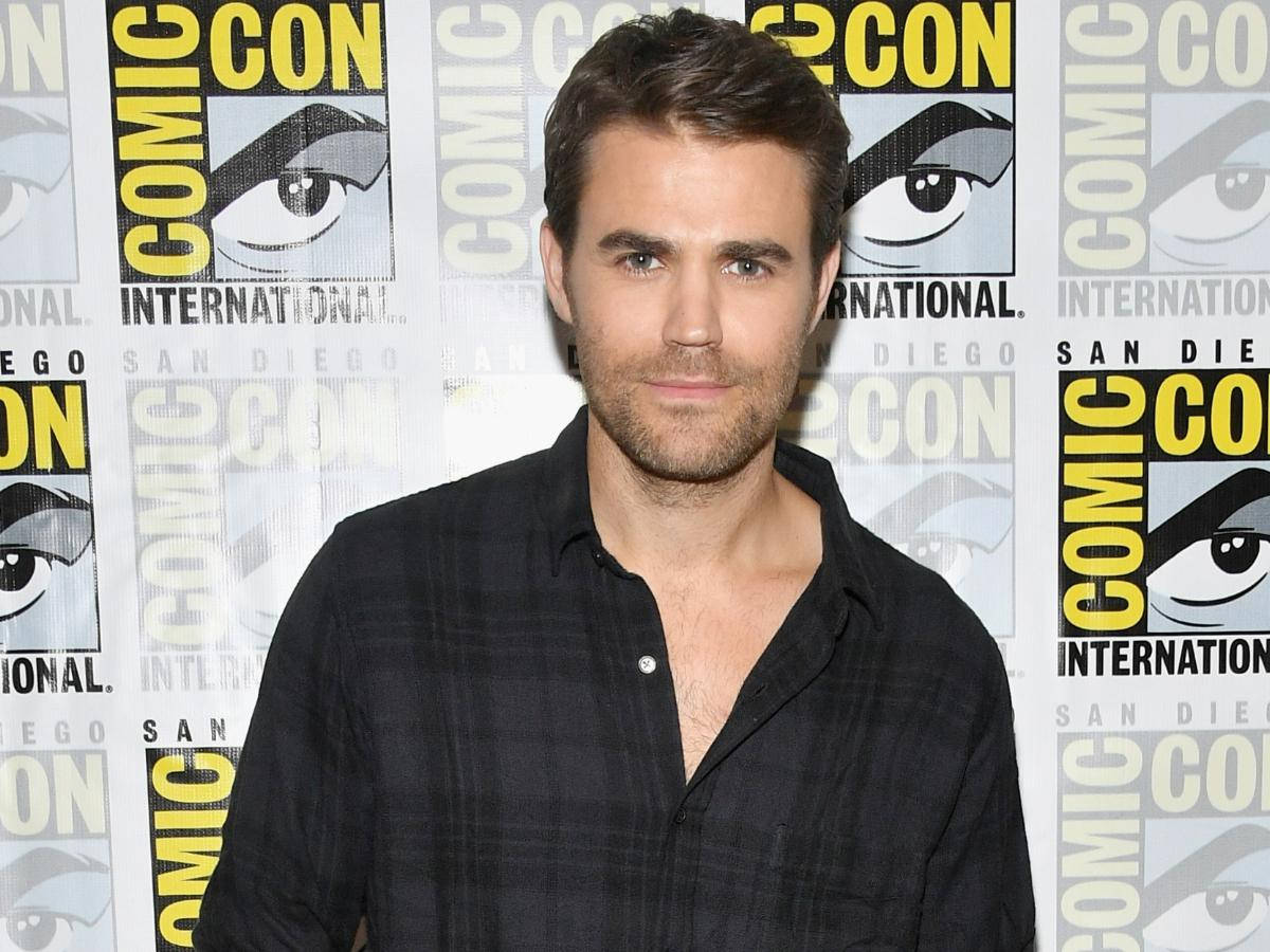 Stefan 桌布 壁紙 — 演員 Paul Wesley 身穿深色格紋襯衫，在重複的 Comic-Con International 背景前擺姿勢，背景上有大型眼睛圖案。
