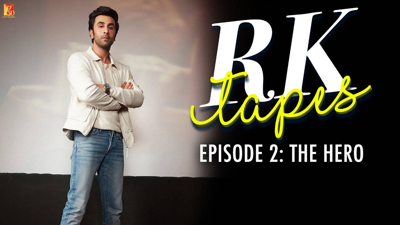 電影動圖 桌布 壁紙 — 演員 Ranbir Kapoor 自信地交叉雙臂，身穿白色外套和牛仔褲，站在帶有粗體「RK Tapes」文字的風格化背景前。
