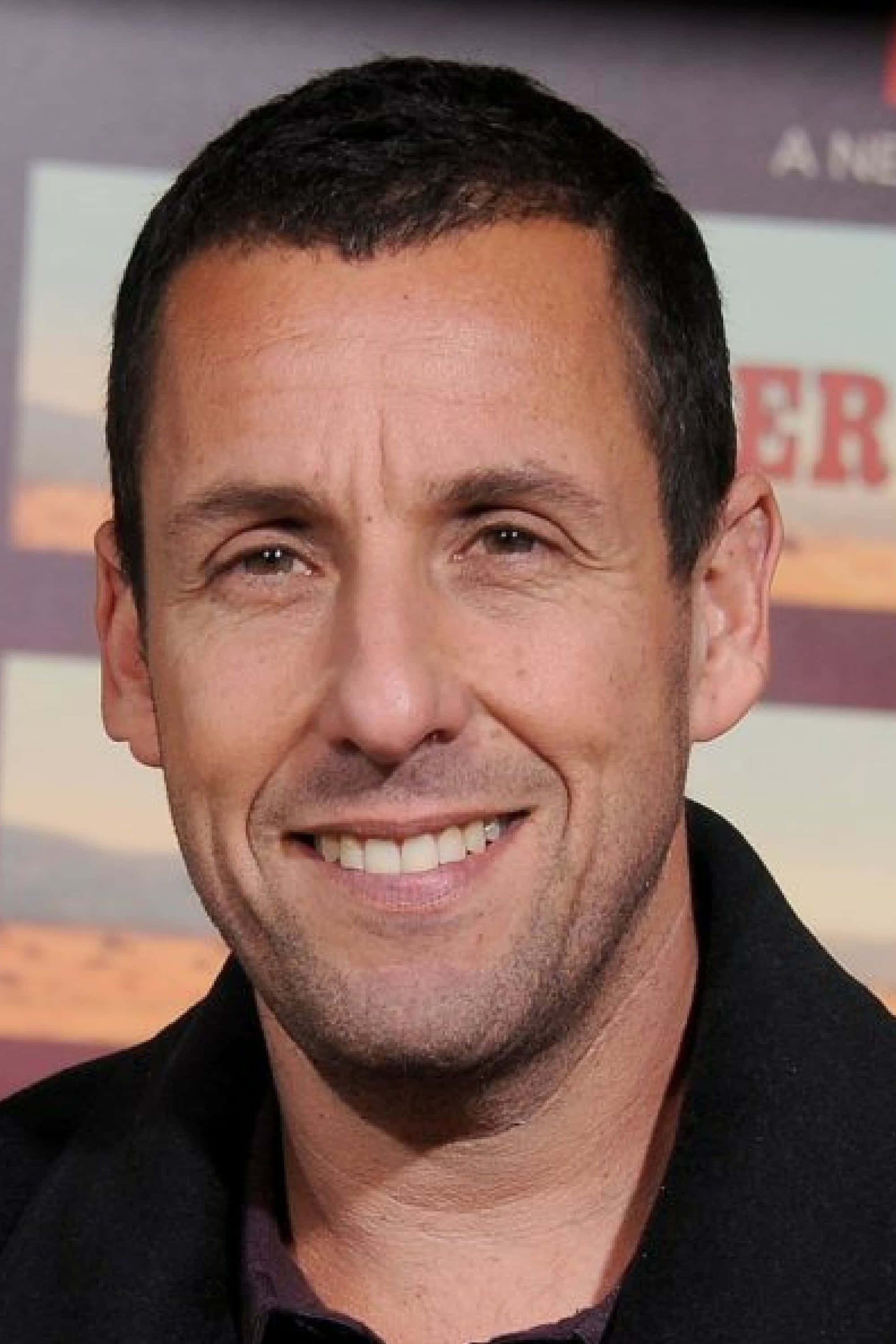 Adam Sandler 桌布 壁紙 — 演員亞當·山德勒在模糊的活動背景前，以特寫肖像照展現溫暖笑容。
