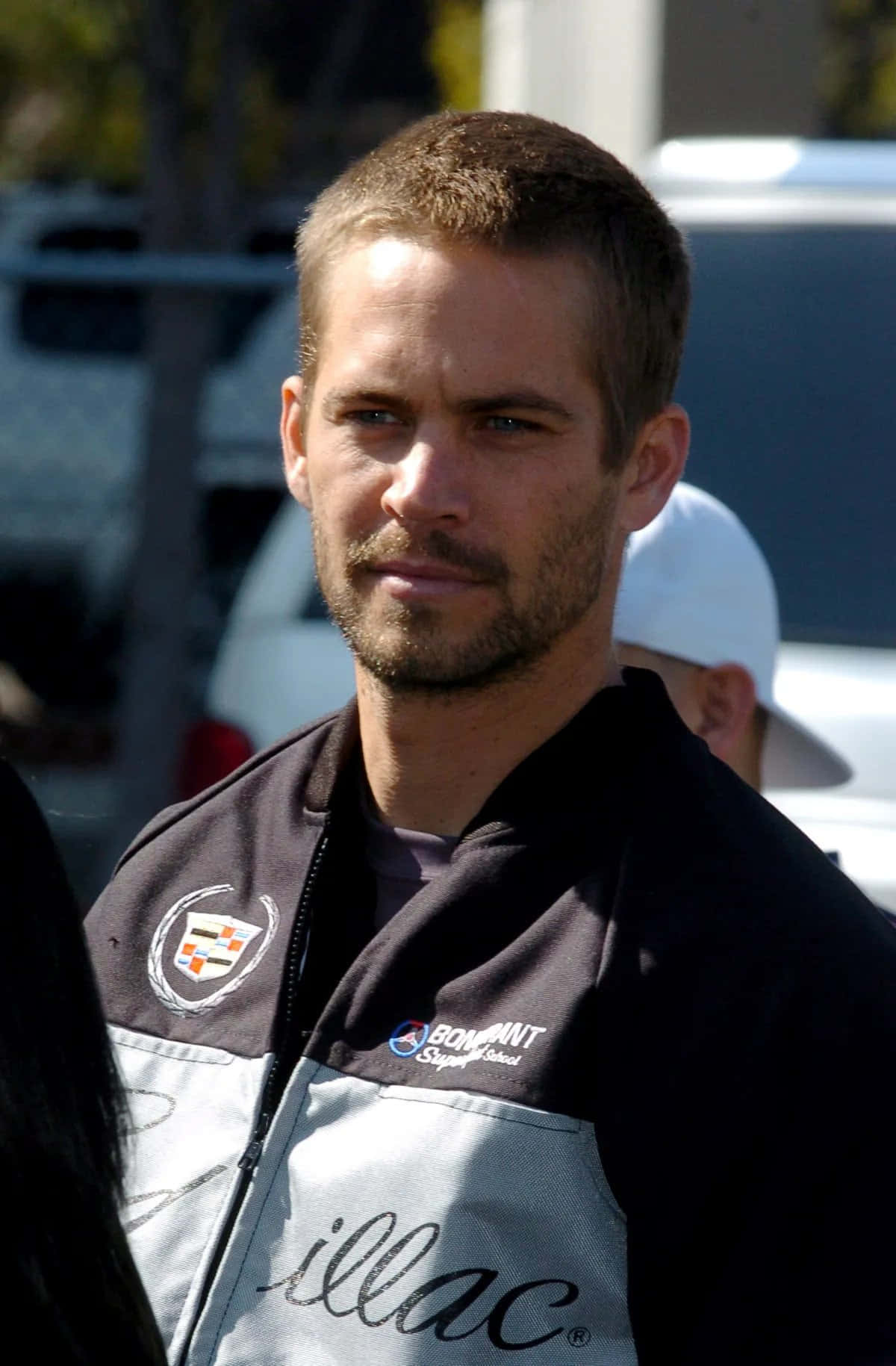 Paul Walker 桌布 壁紙 — 演員保羅·沃克身穿凱迪拉克賽車外套，在明亮陽光下以嚴肅表情直視鏡頭。