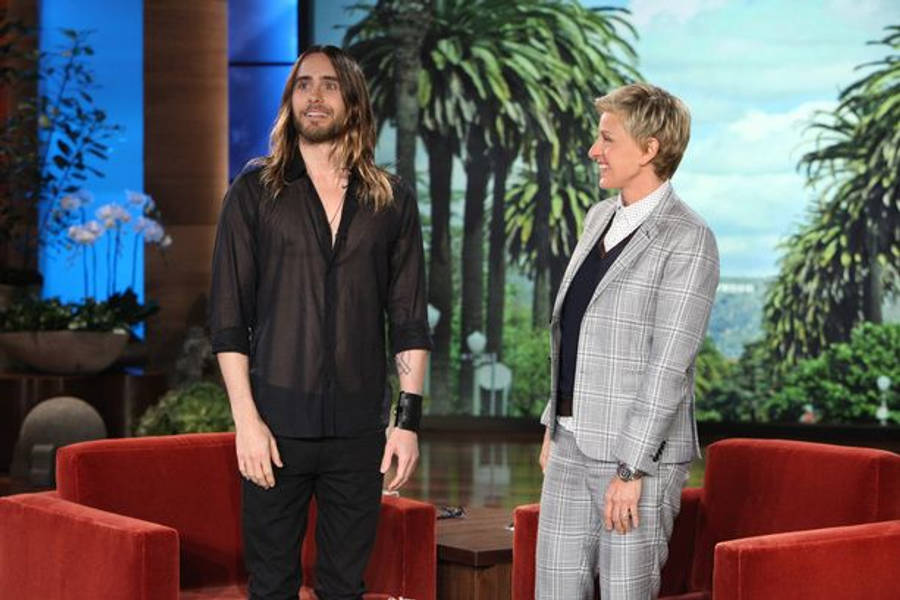 the ellen show 桌布 壁紙 — 演員傑瑞德·雷托站在主持人艾倫·狄珍妮旁邊，在一個有紅色椅子和棕櫚樹背景的脫口秀場景中。