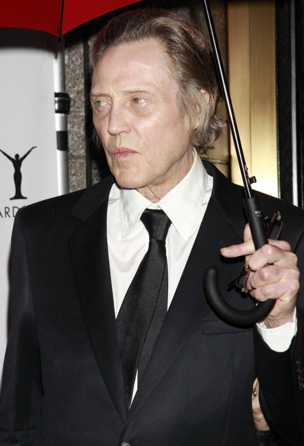 Celebrity 桌布 壁紙 — 演員克里斯多福·沃肯穿著黑色西裝，在白色背景的活動中拿著一把關閉的紅色雨傘。