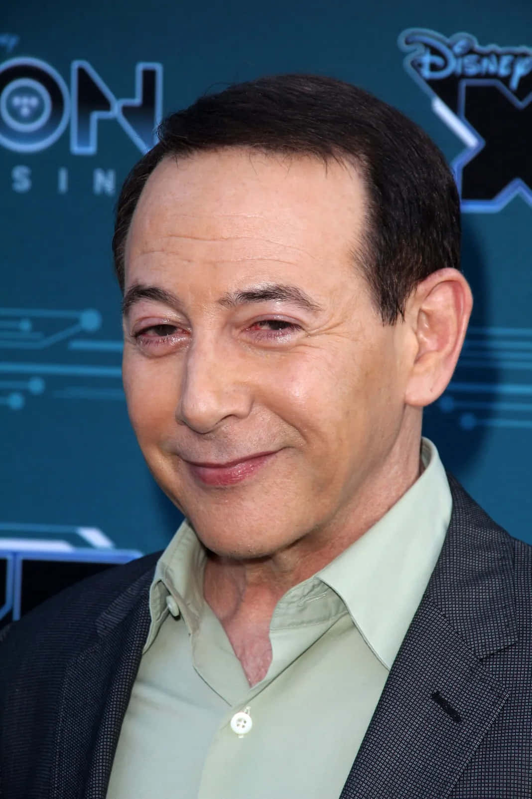 Paul Reubens 桌布 壁紙 — 演員凱文·史貝西在迪士尼活動中穿著深色西裝和淺綠色襯衫，溫暖地微笑。