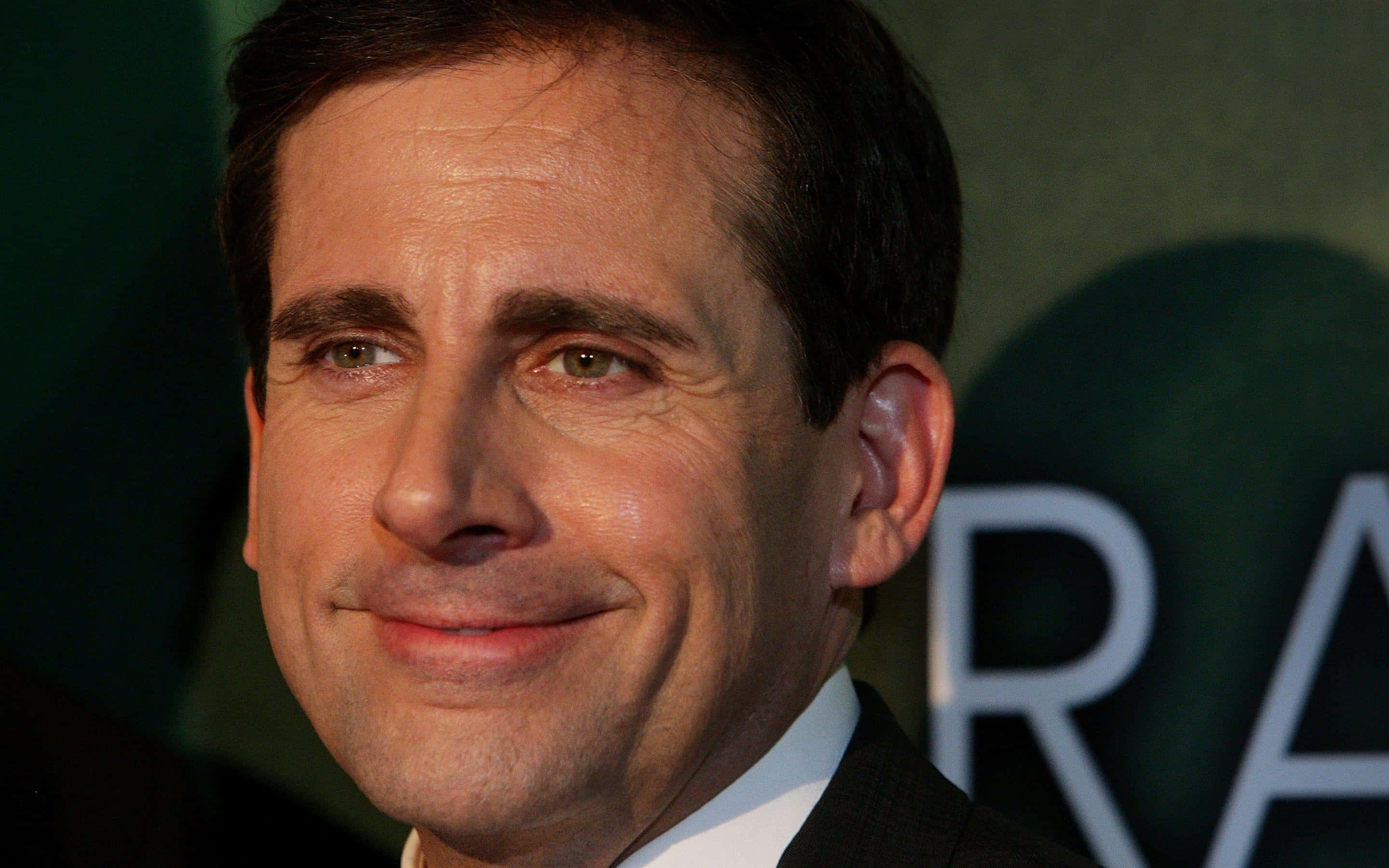 steve carell 桌布 壁紙 — 演員史提夫·卡爾身穿深色西裝，在模糊的綠色背景和部分白色文字前溫暖微笑的特寫肖像。